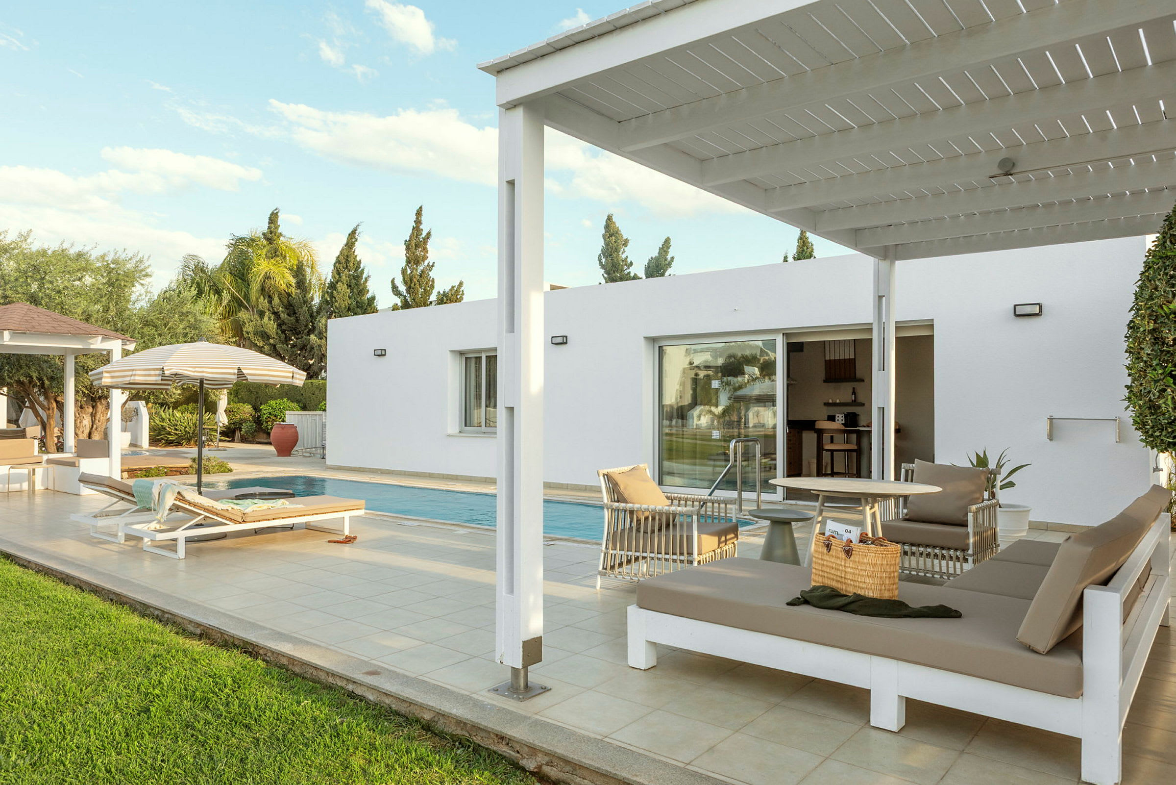 Utendørsområde med et basseng, solsenger og en pergola ved siden av en moderne bygning. (AI-generert tekst)