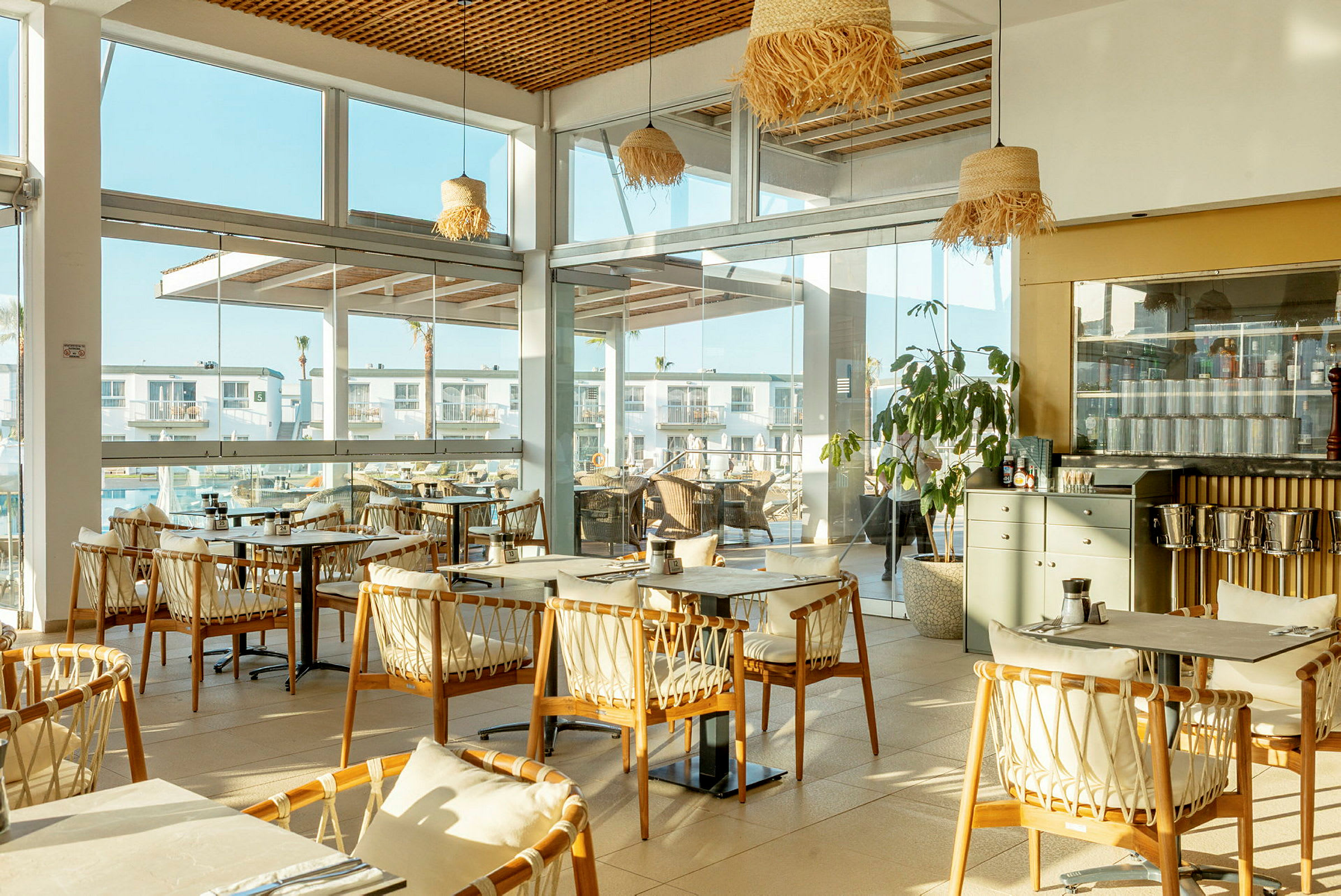 En restaurant med store vinduer og trestoler rundt bordene. (AI-generert tekst)
