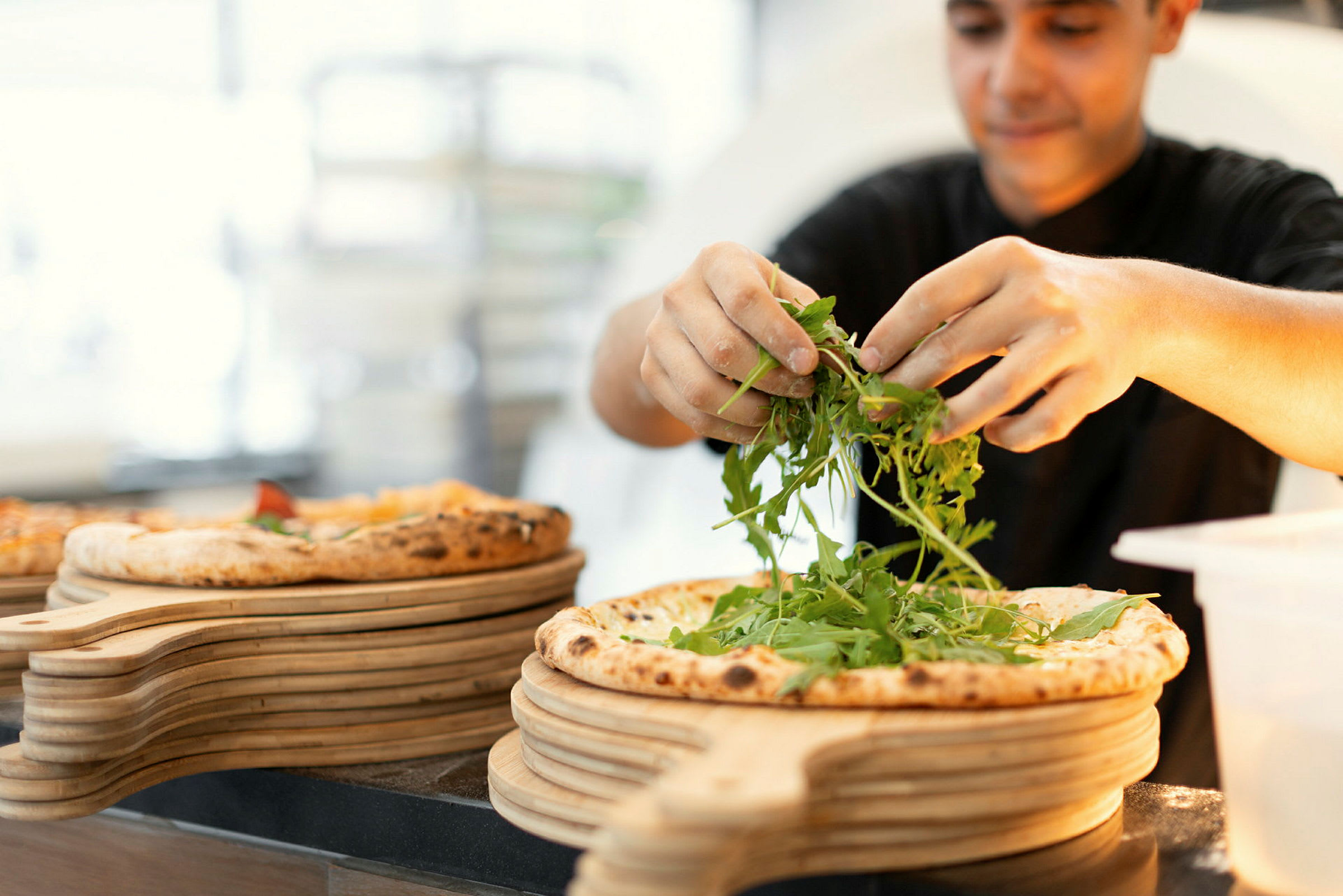 En person pynter en pizza med ruccolasalat. (AI-generert tekst)