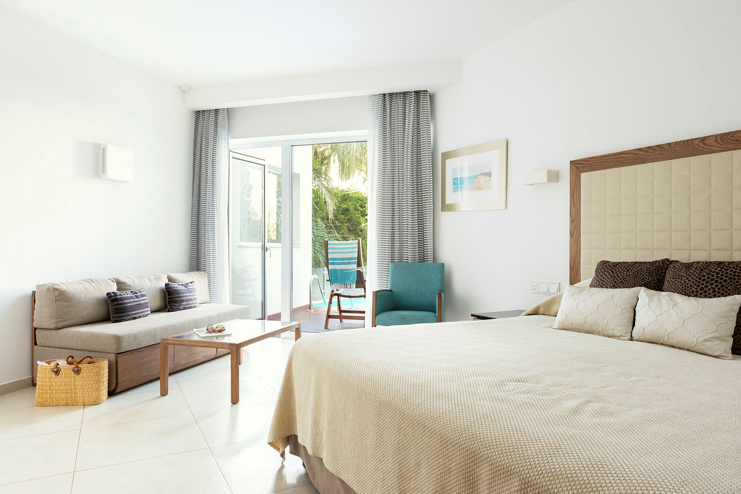 Hotellrom med seng, sofa og utsikt mot en terrasse med hage. (AI-generert tekst)