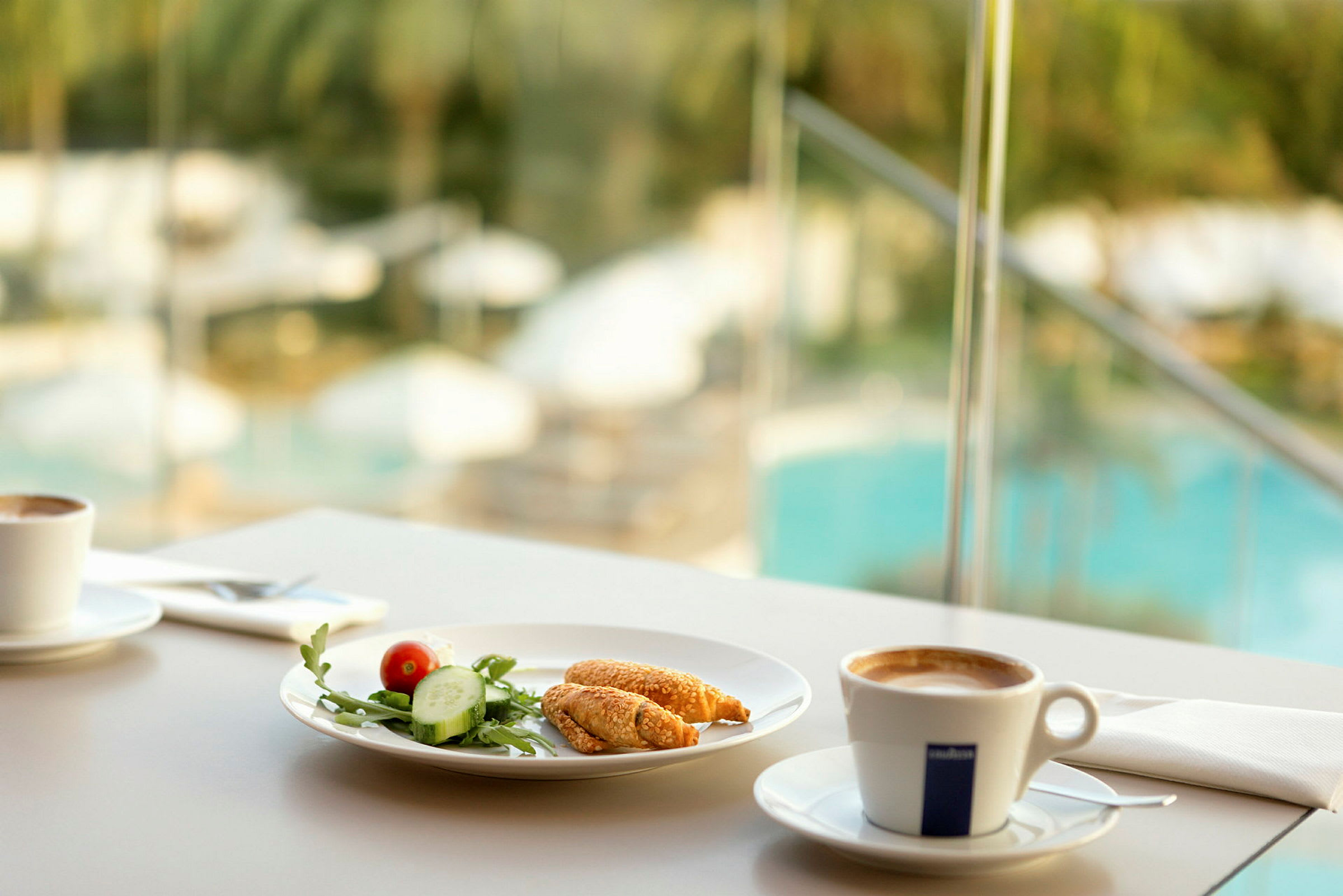 Frokostservering med kaffe og en tallerken med grønnsaker og bakverk, bakgrunn med utsikt over et basseng. (AI-generert tekst)