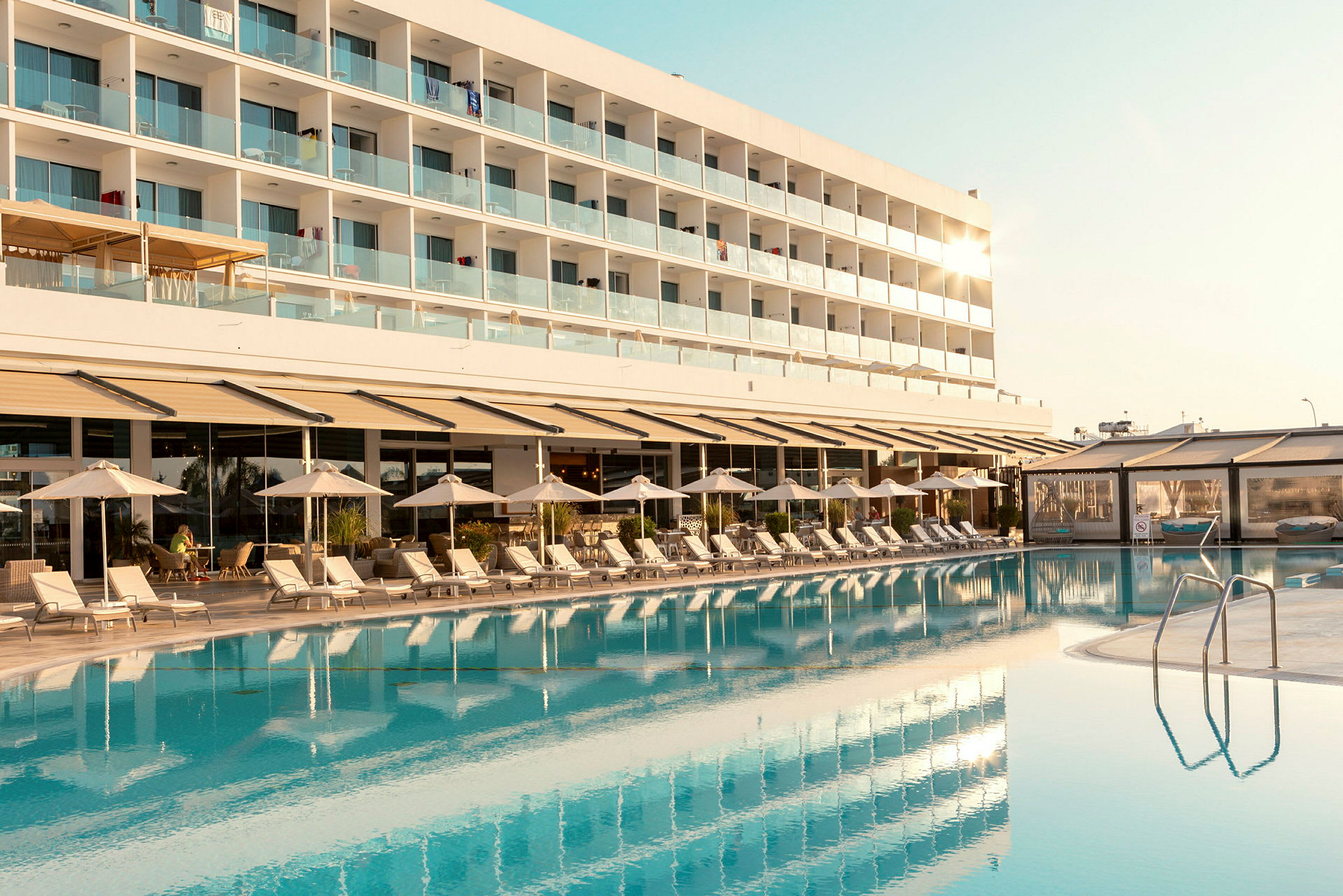 En hotellbygning med balkonger kan sees bak et basseng og solsenger. (AI-generert tekst)