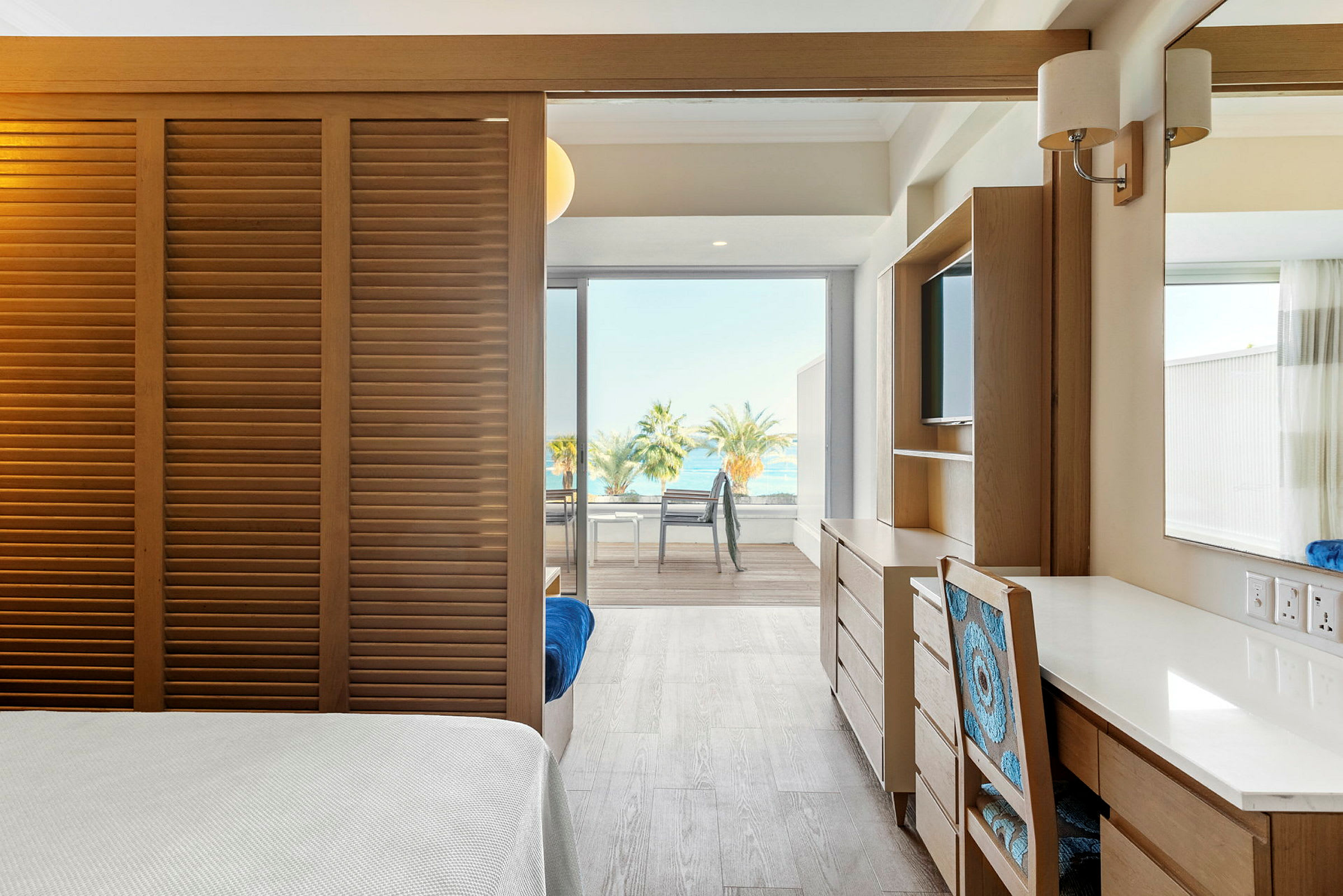 Et lyst hotellrom med utsikt over havet og palmer gjennom store vinduer. (AI-generert tekst)