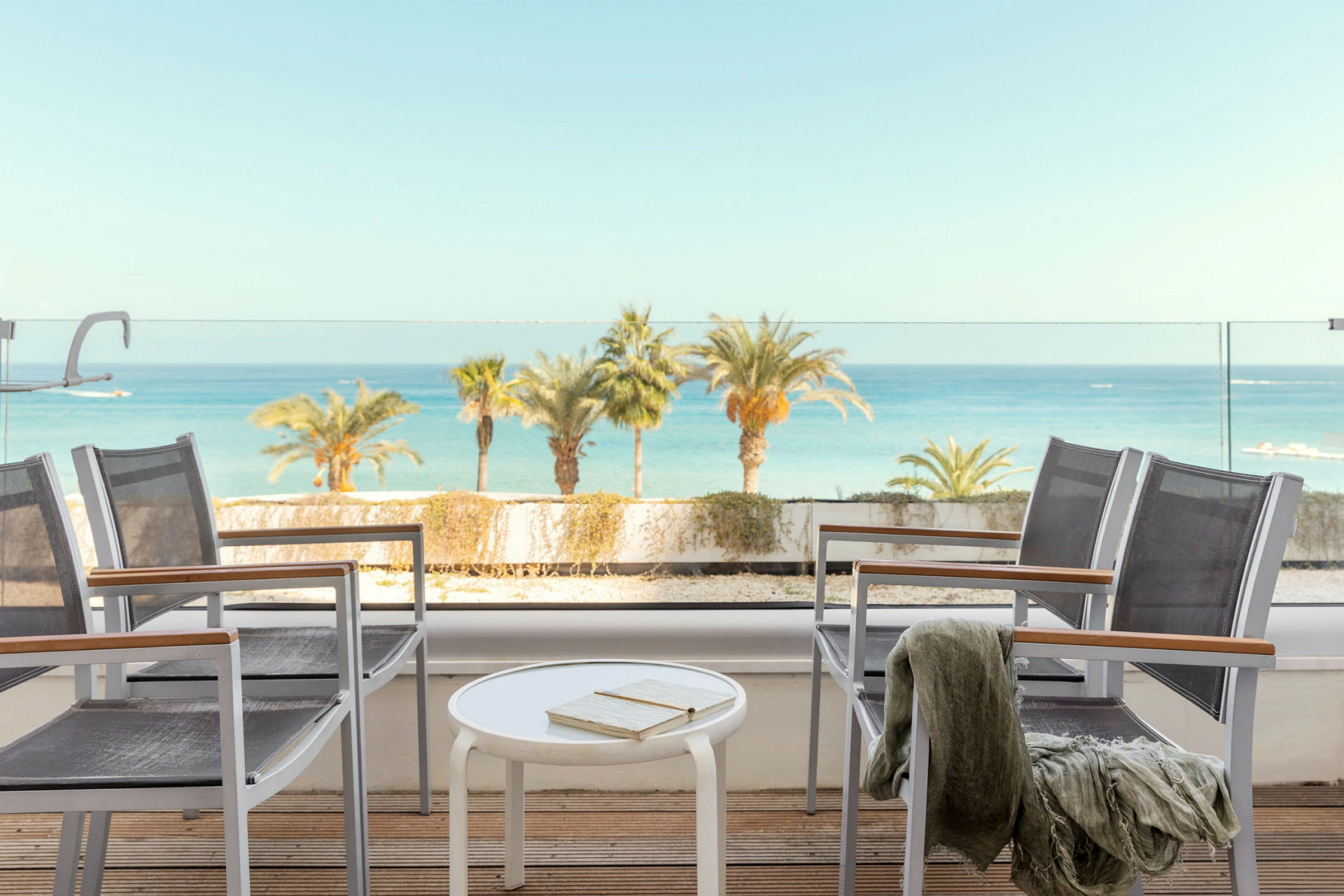 Utsikt fra en terrasse med stoler, bord og havet i bakgrunnen. (AI-generert tekst)