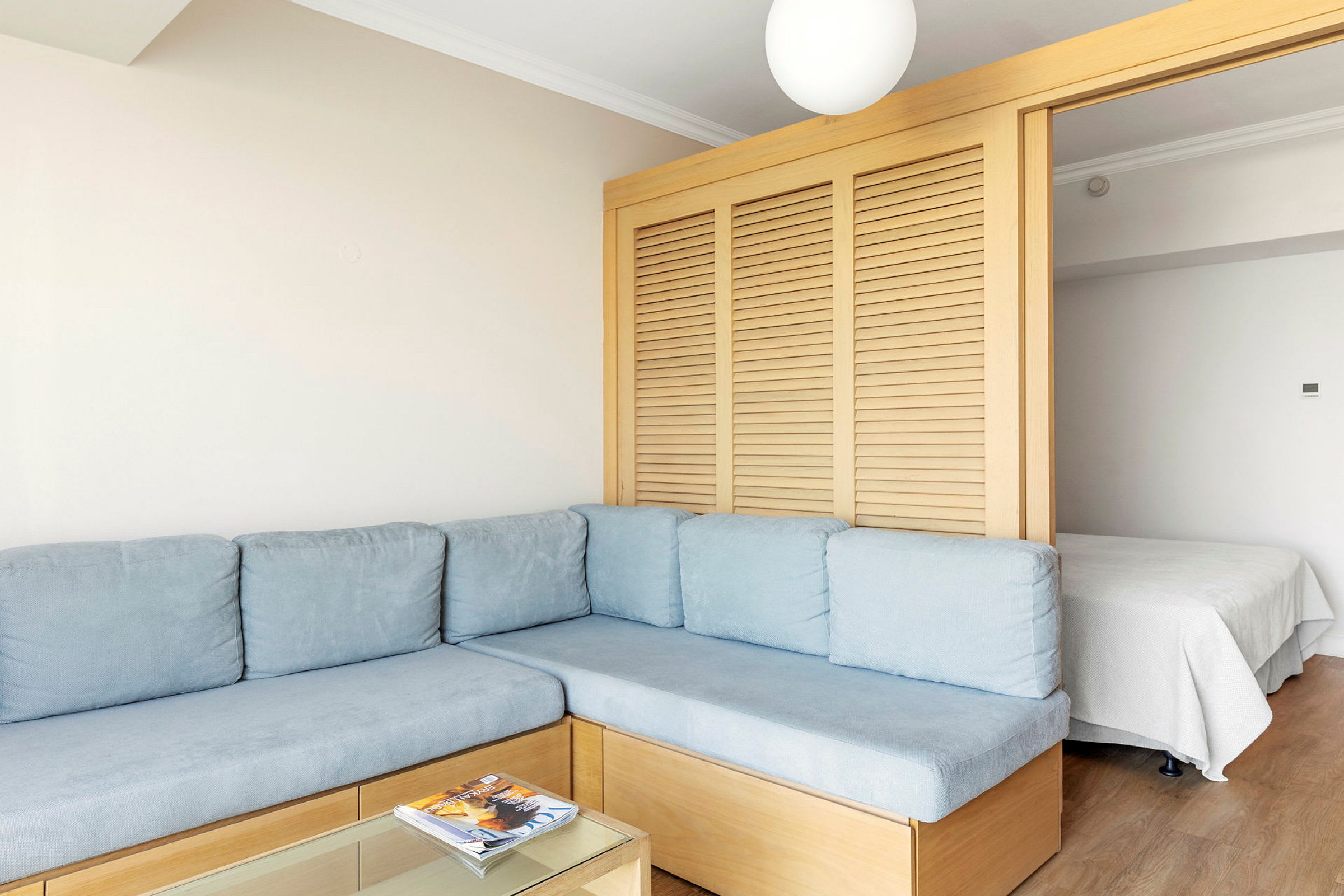 Et rom med en hjørnesofa, et lavt bord med blader og en skillevegg som deler av en soveplass. (AI-generert tekst)