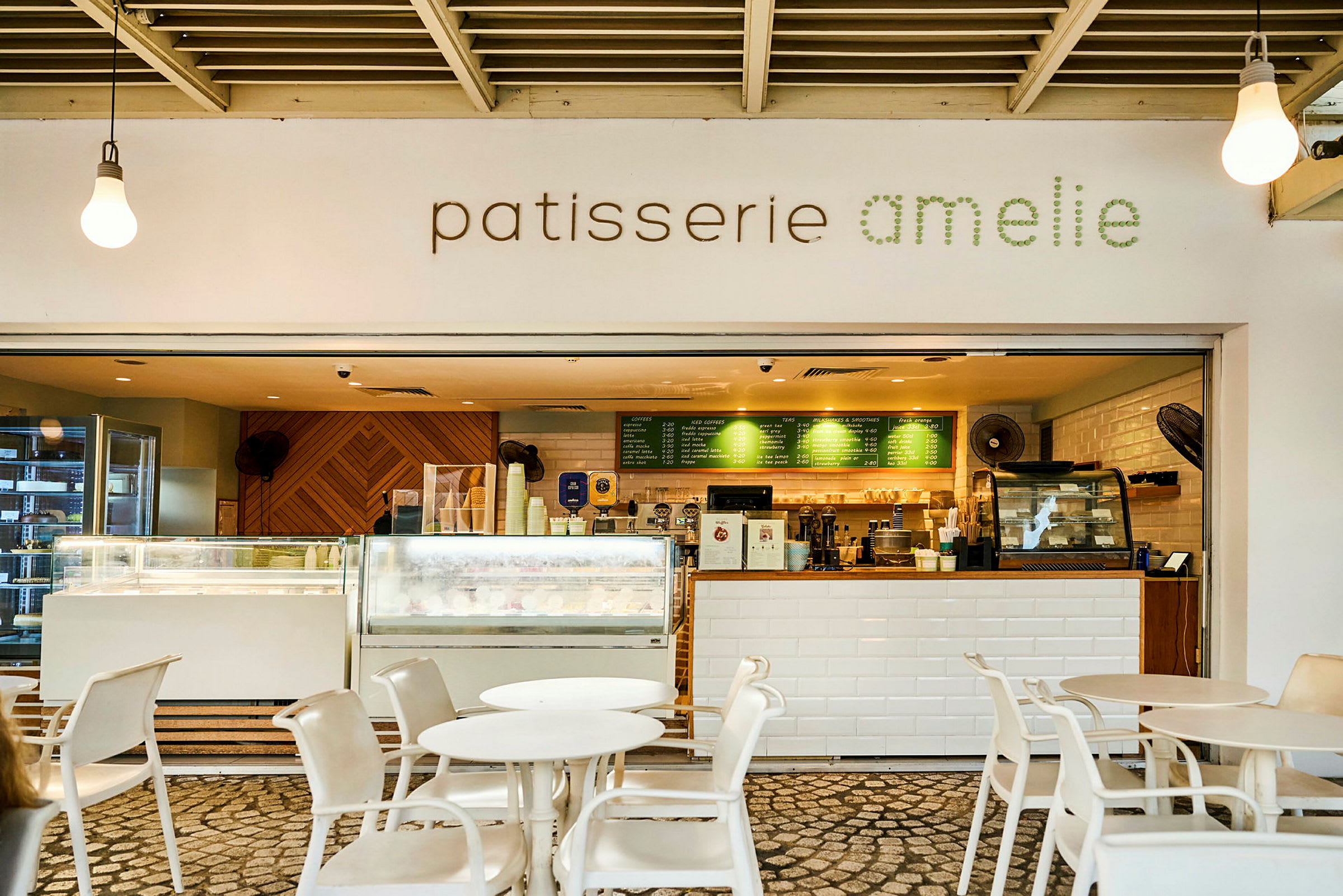 En kafé med skiltet "patisserie amelie" og en innbydende serveringsdisk med bord og stoler foran. (AI-generert tekst)