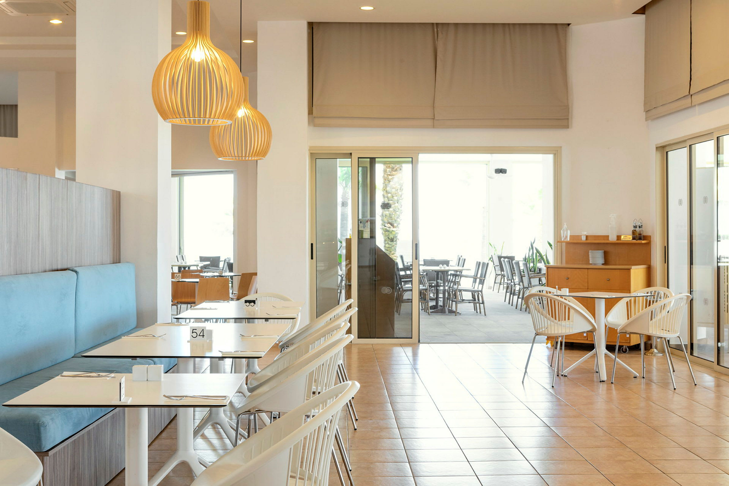 Interiør av en lys restaurant med bord og stoler, samt taklamper. (AI-generert tekst)