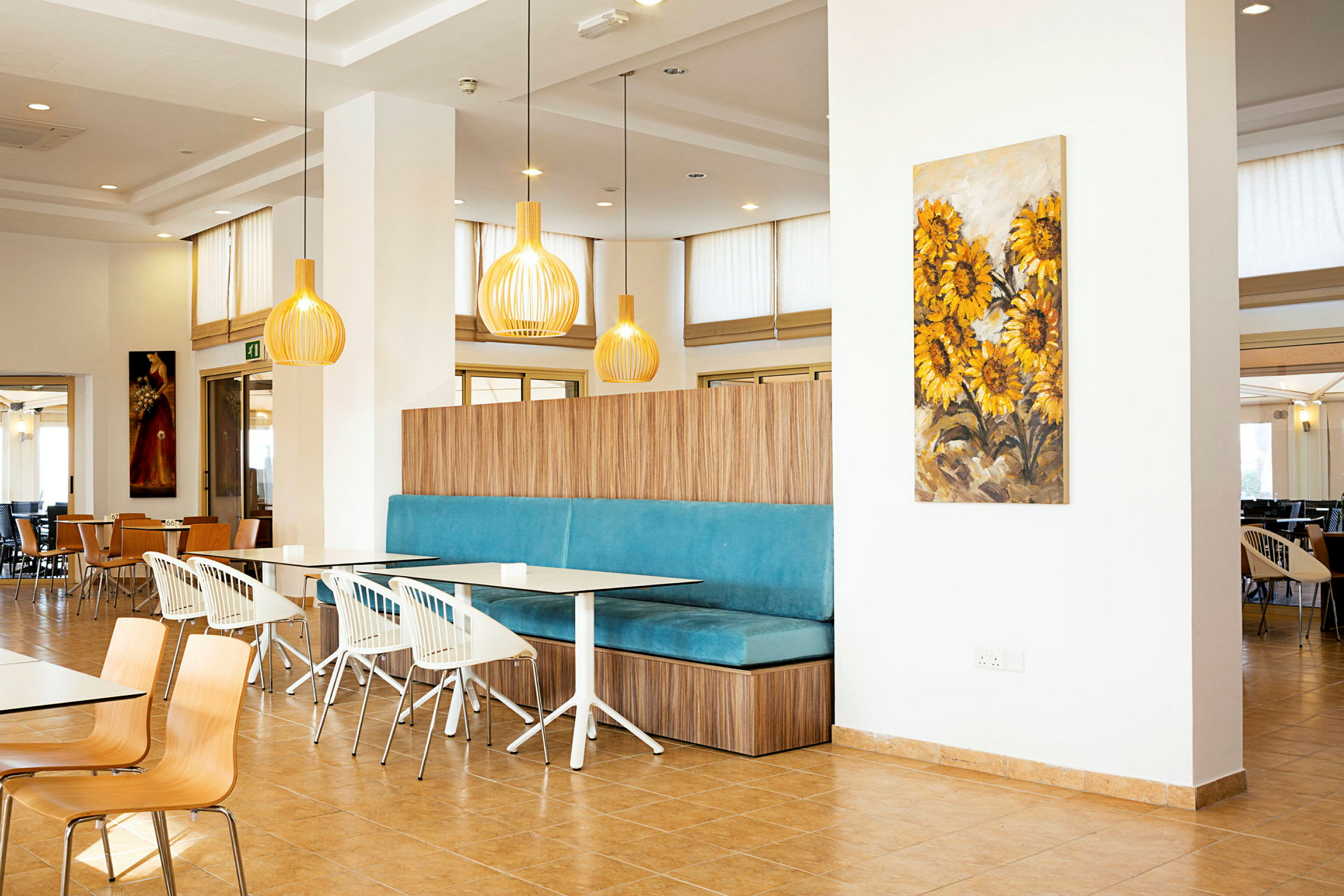 Interiør av en restaurant med moderne innredning og fargerik veggkunst med solsikkemotiv. (AI-generert tekst)