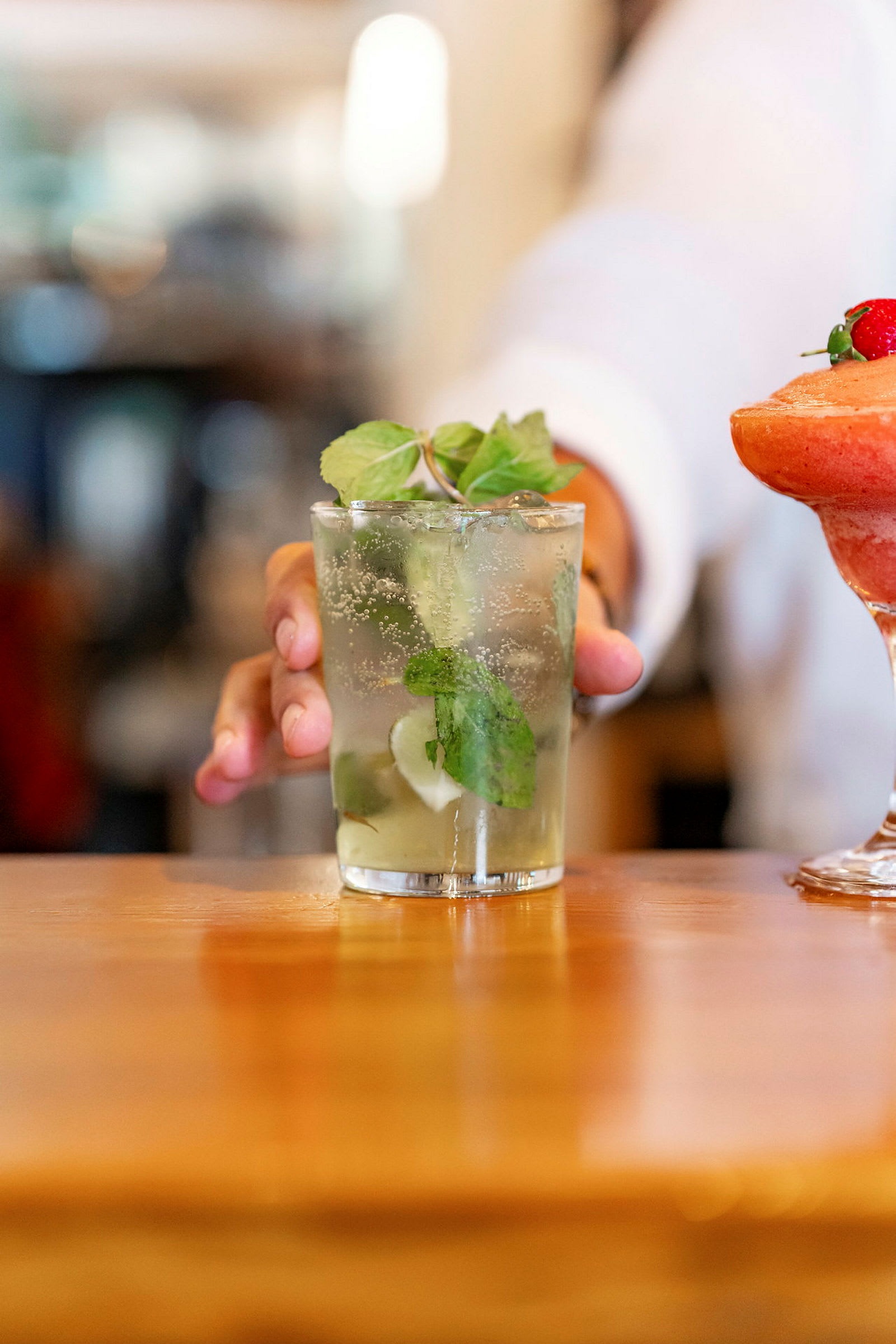 En person serverer en drink med mynteblader på et bord. (AI-generert tekst)