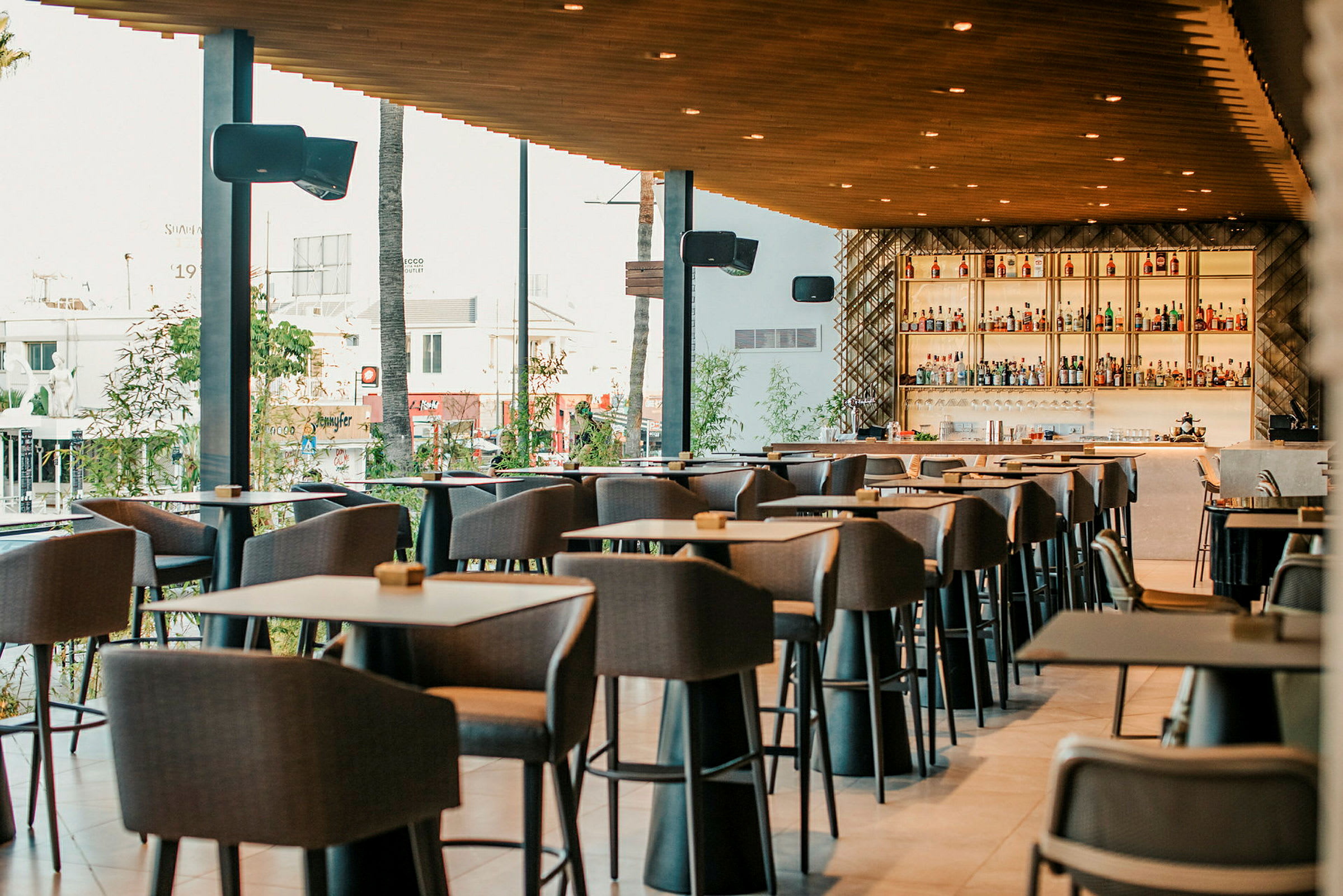 Bilde av en moderne restaurant med høye bord og stoler samt en velfylt bar i bakgrunnen. (AI-generert tekst)