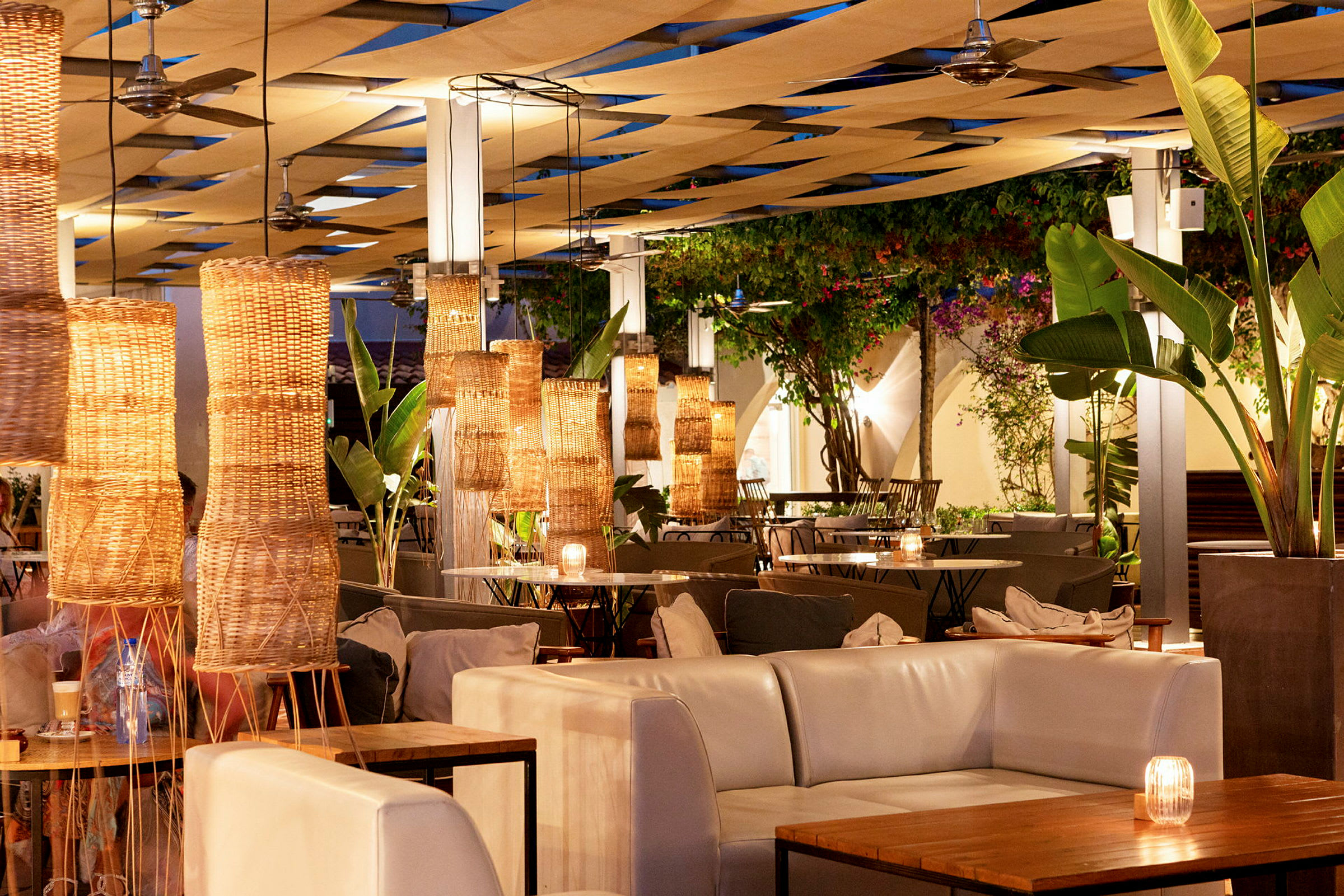 En utendørs restaurant med lysdekorasjoner i kurvlamper og planteinteriør. (AI-generert tekst)