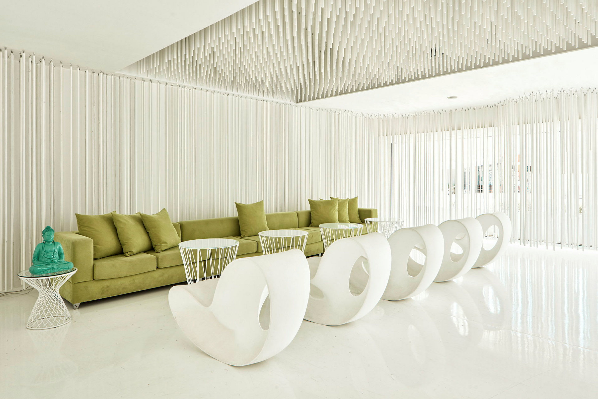 En moderne lounge med grønn sofa, hvite stoler og et bord med en turkis Buddha-statue. (AI-generert tekst)