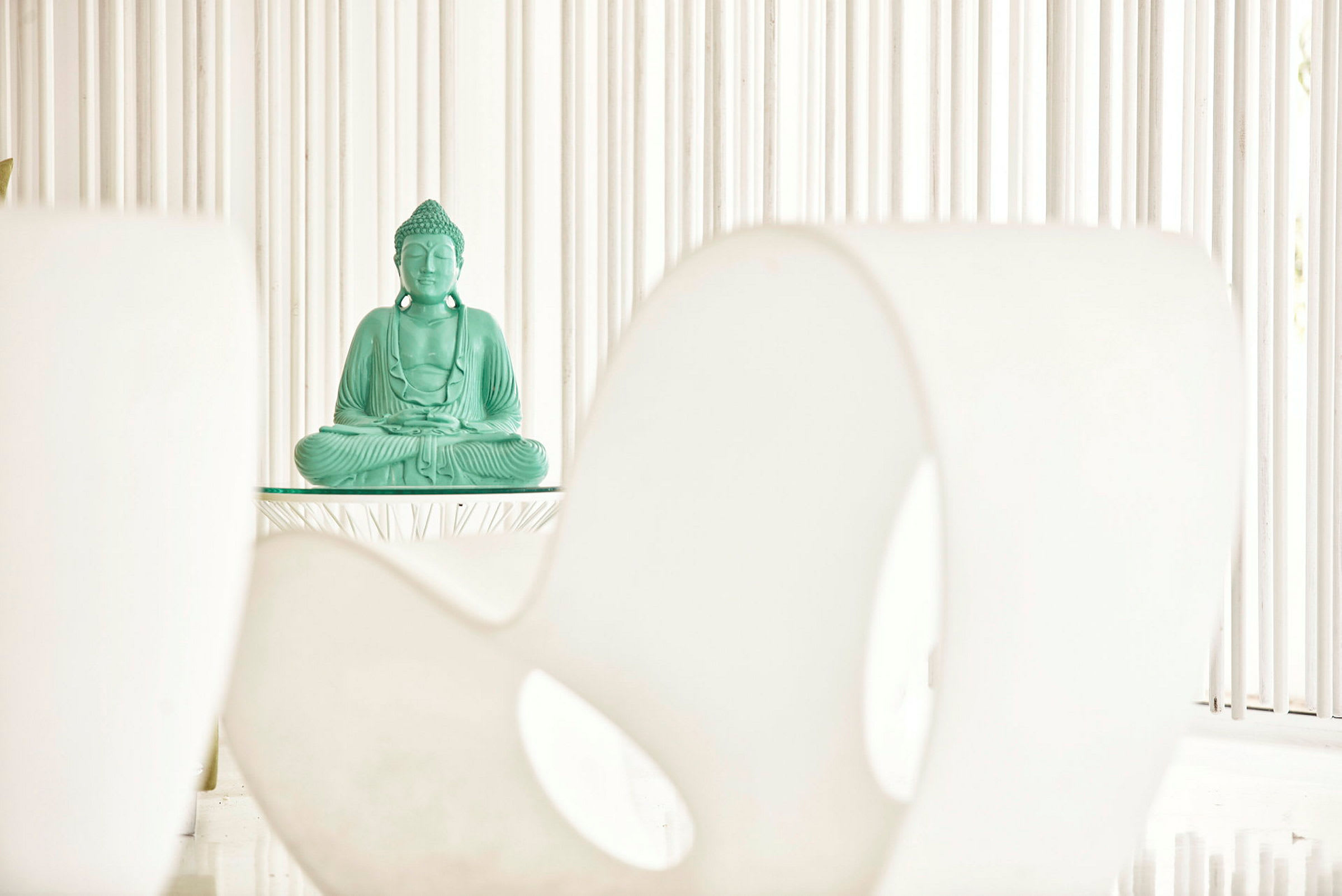 En grønn Buddha-statue plassert på et bord mot en minimalistisk bakgrunn. (AI-generert tekst)