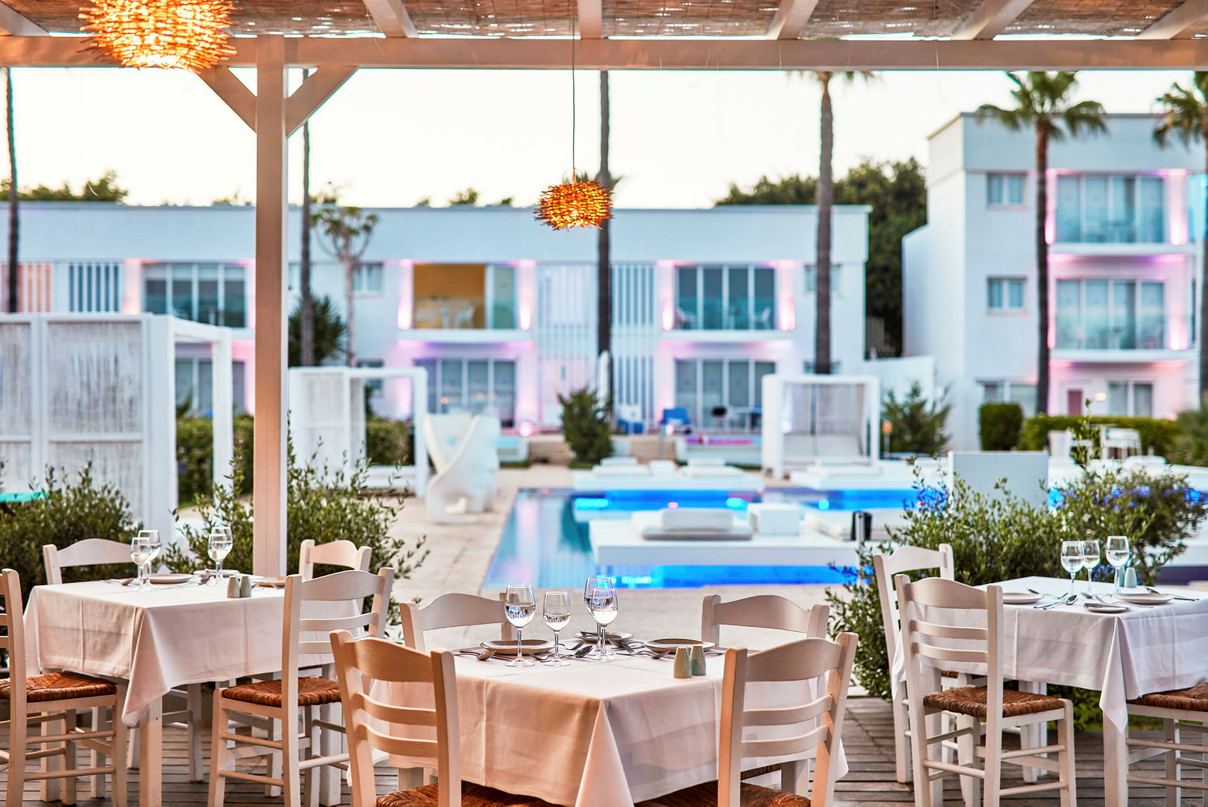 Restaurant med dekkede bord ved bassenget med moderne bygninger i bakgrunnen. (AI-generert tekst)