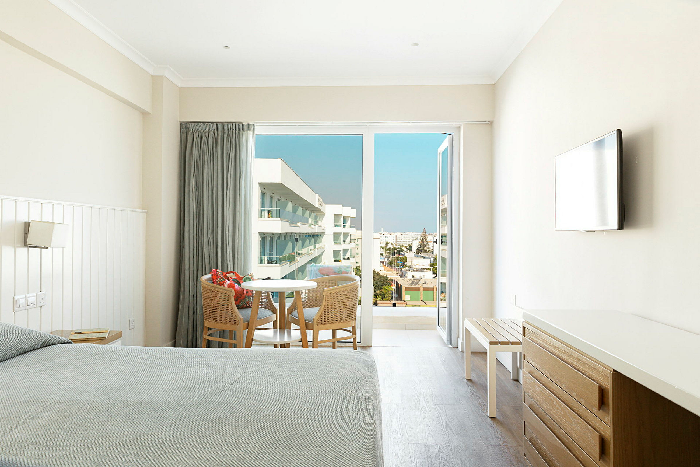 Hotellrom med sittegruppe og åpne balkongdører med utsikt over omgivelsene. (AI-generert tekst)
