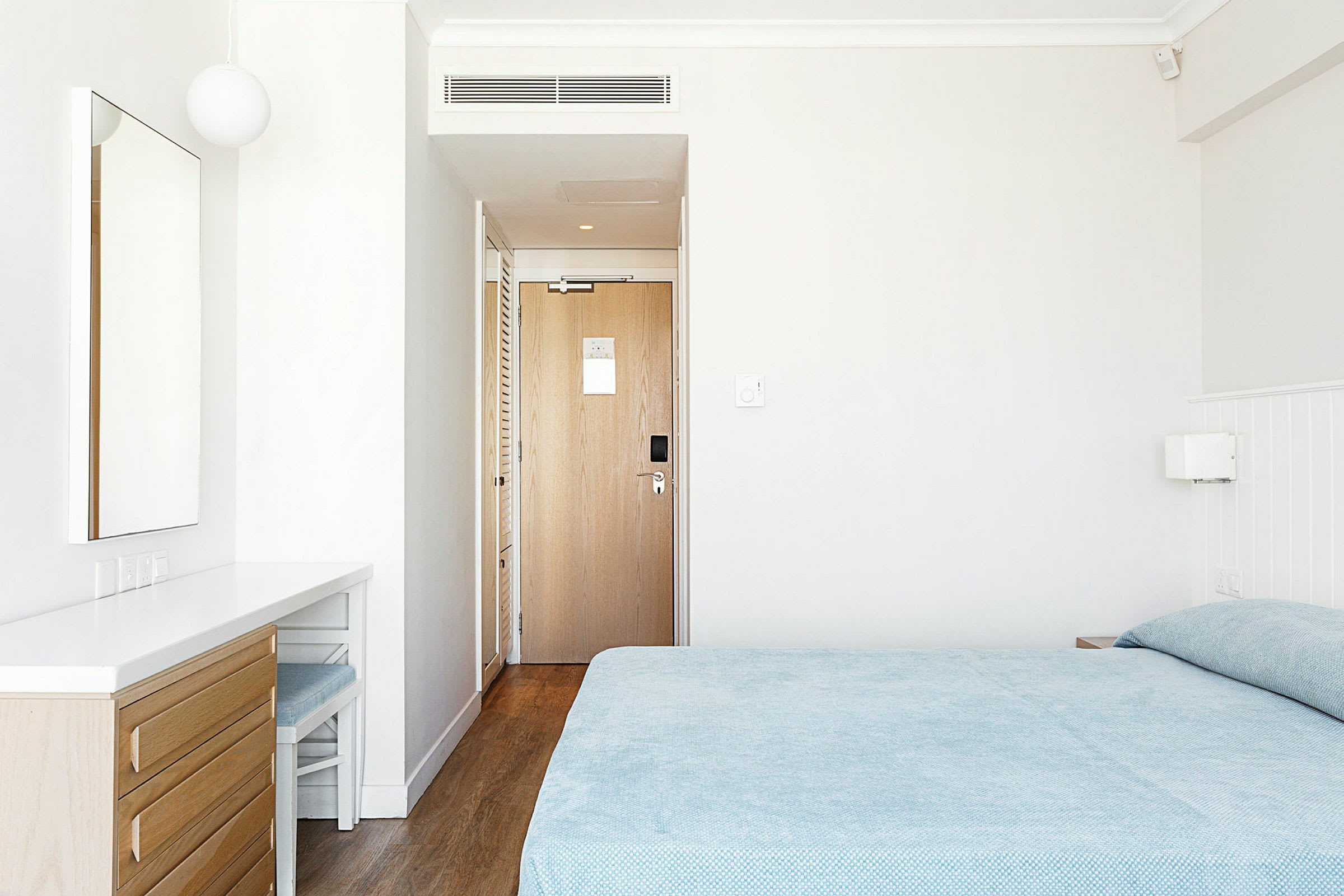 Et hotellrom med en seng, et speil på en kommode og en dør. (AI-generert tekst)