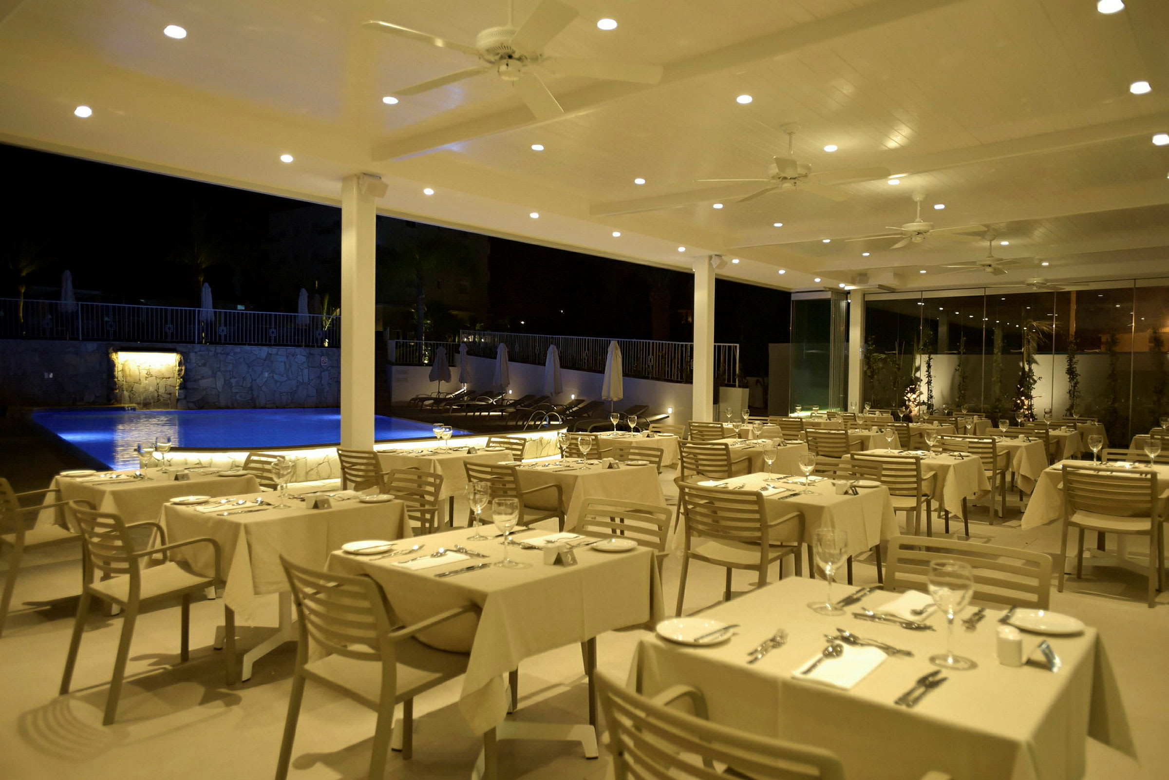 Restaurant med dekkede bord ved et basseng om kvelden. (AI-generert tekst)
