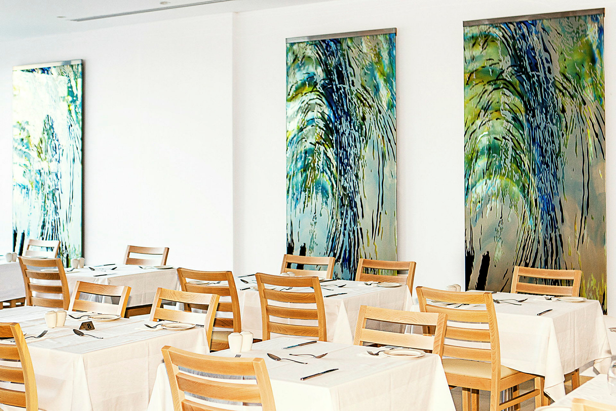 En restaurant med dekkede bord og trestoler mot vegger dekorert med fargerike kunstverk. (AI-generert tekst)
