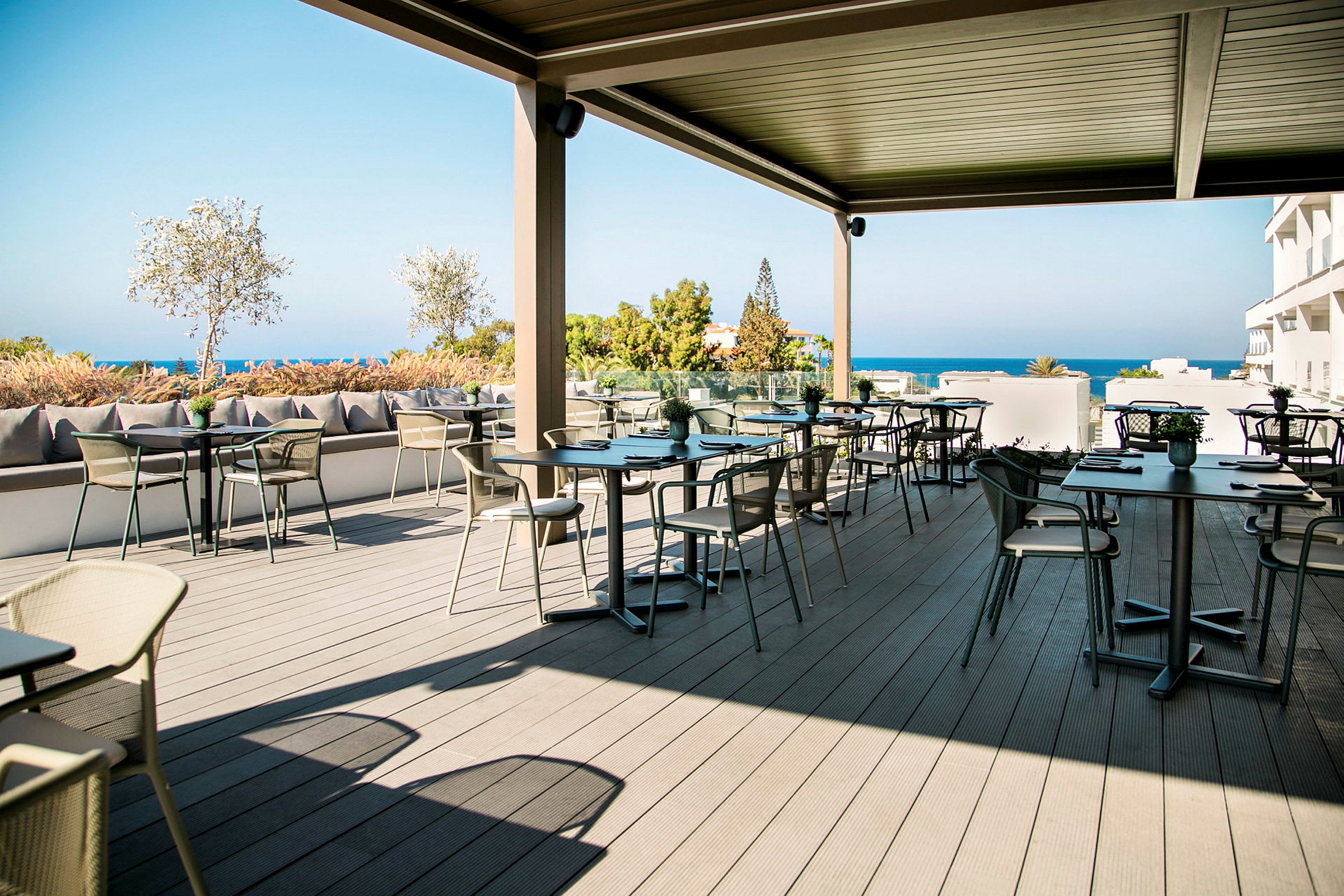 En utendørs kafé med bord og stoler på en terrasse med utsikt over havet. (AI-generert tekst)