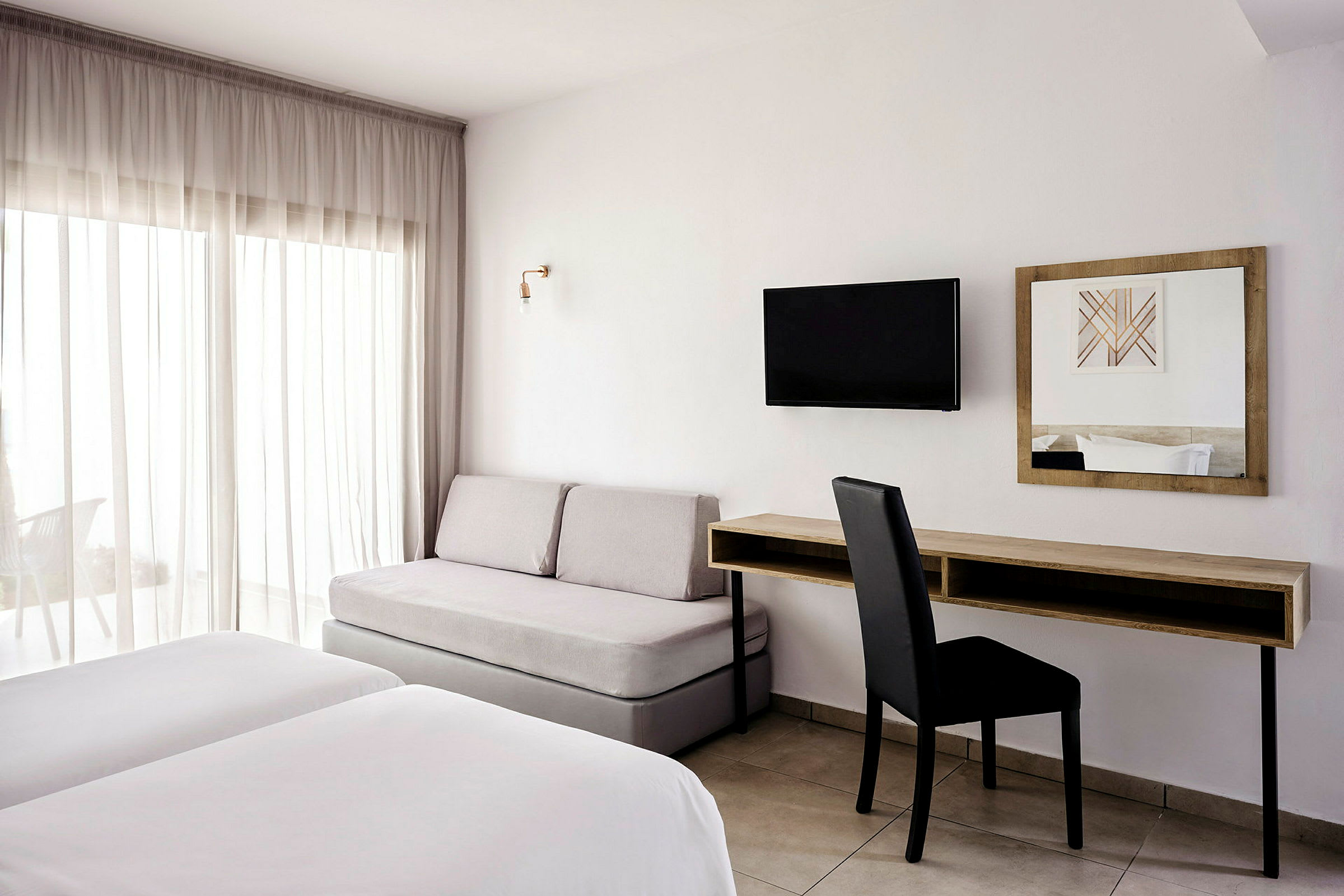 Et hotellrom med to senger, en sofa, et skrivebord og en veggmontert TV. (AI-generert tekst)
