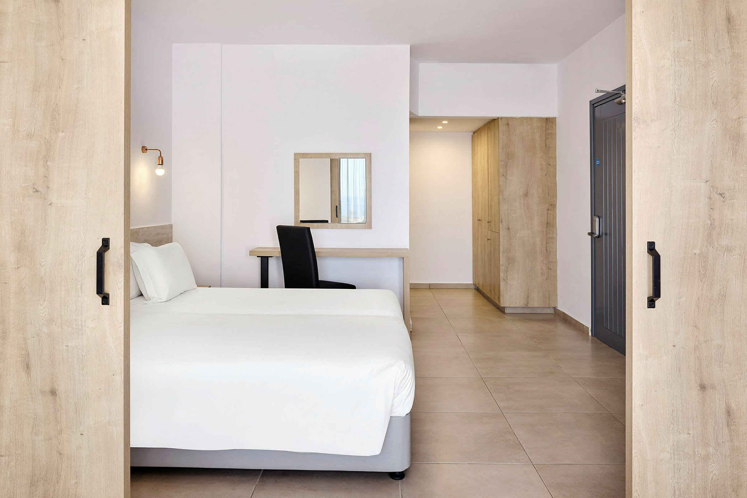 Et hotellrom med en dobbeltseng, skrivebord, speil og oppbevaringsmøbler. (AI-generert tekst)