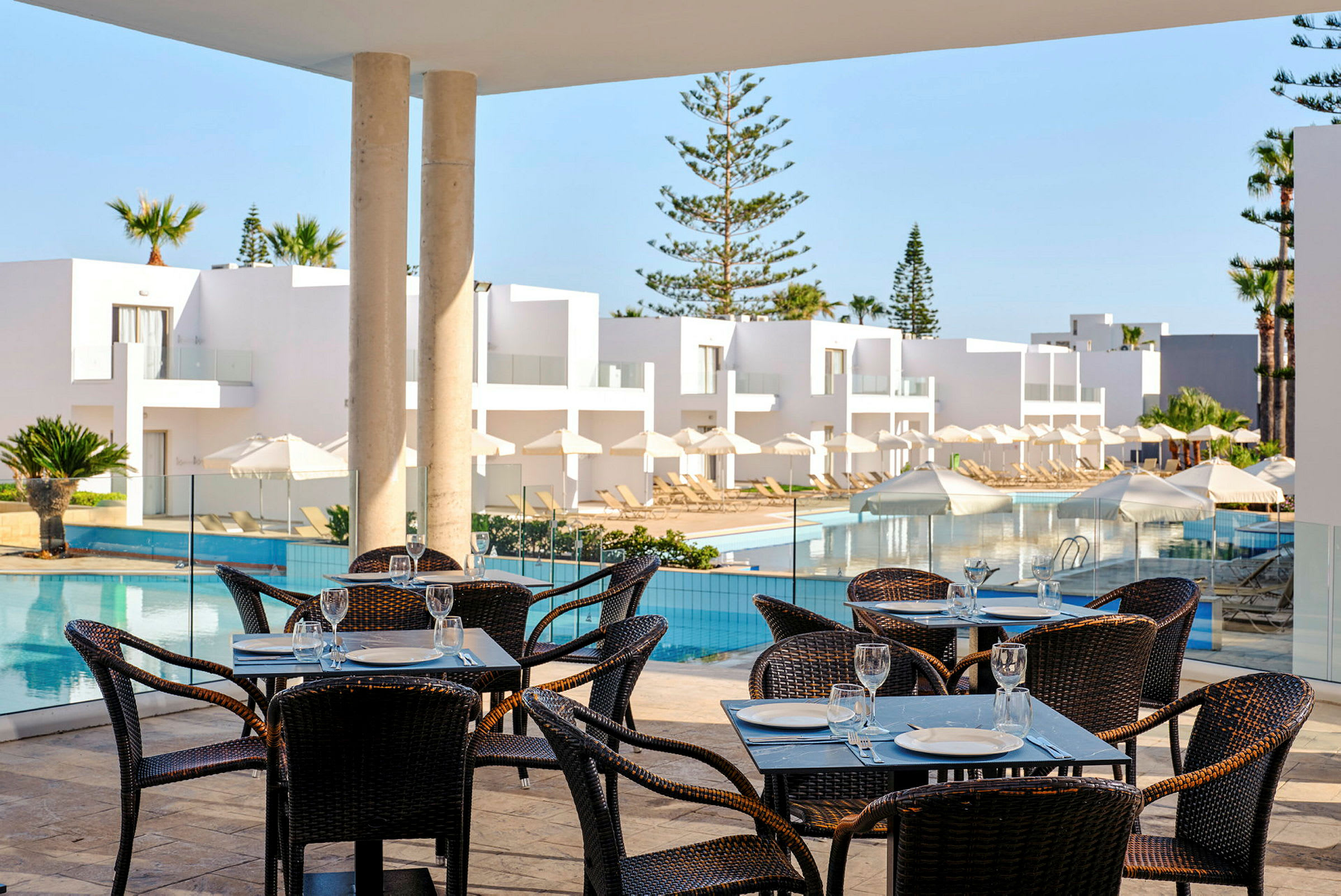 Restaurant med bord og stoler ved en terrasse med bassengområde. (AI-generert tekst)