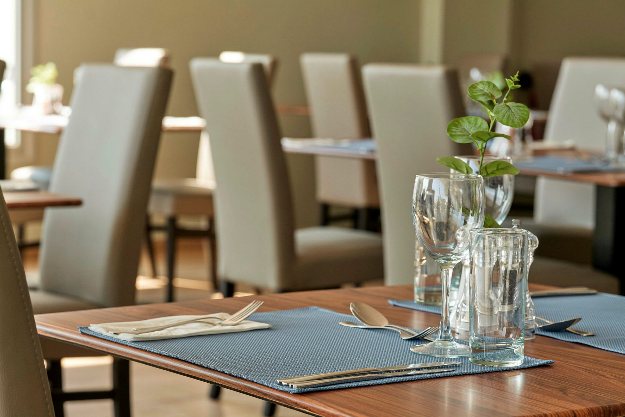Et dekket bord med glass, bestikk og en grønn plante på en restaurant. (AI-generert tekst)