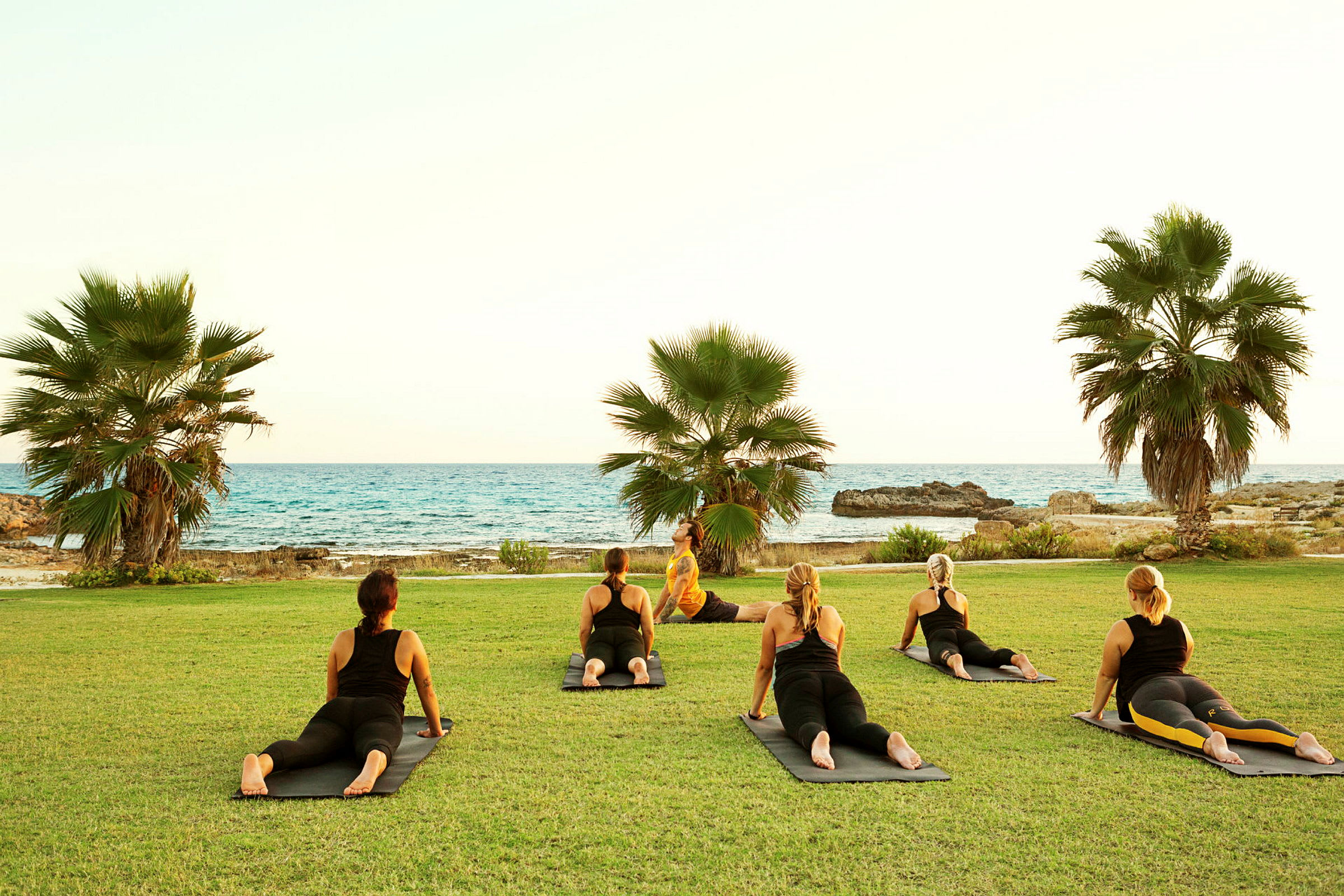 Folk driver med yoga på gresset med utsikt over havet og palmer. (AI-generert tekst)