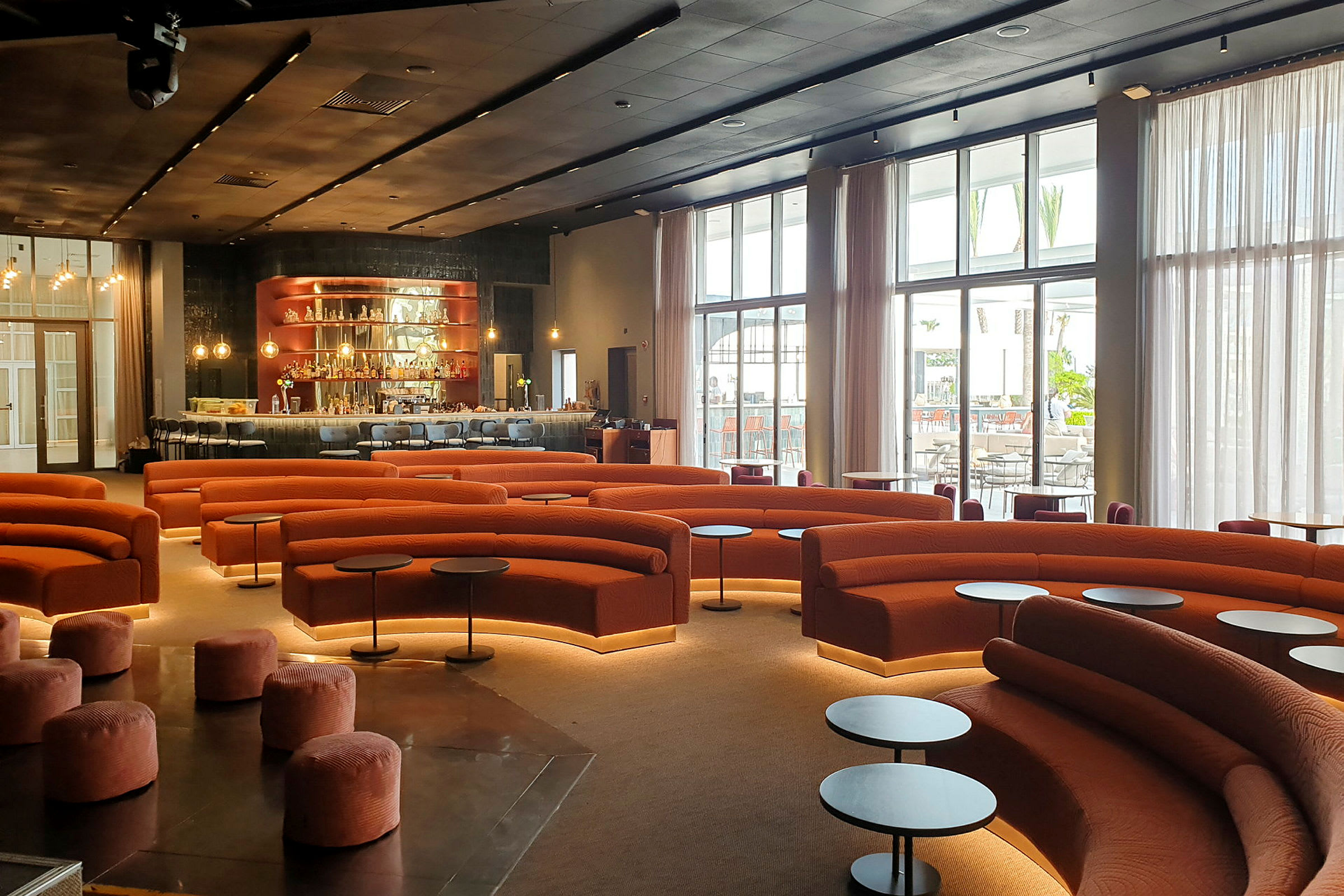 En moderne lounge med oransje sofaer, runde småbord og en bardisk i bakgrunnen. (AI-generert tekst)