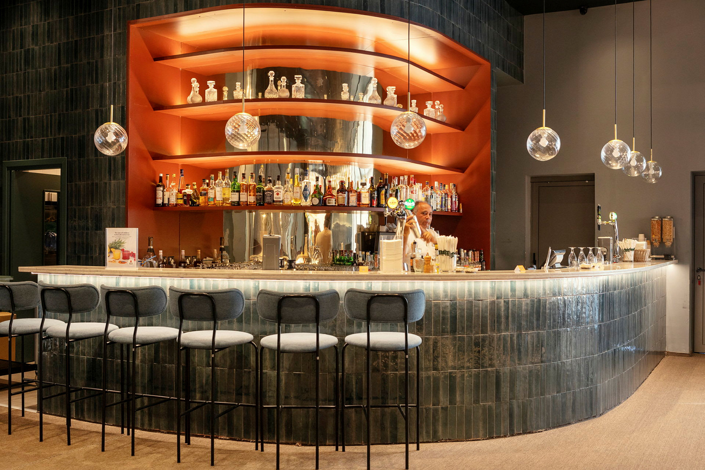 En moderne bar med benkeplate i lys stein og hyller med brennevinsflasker, dekorasjoner og hengende glasskuppler. (AI-generert tekst)