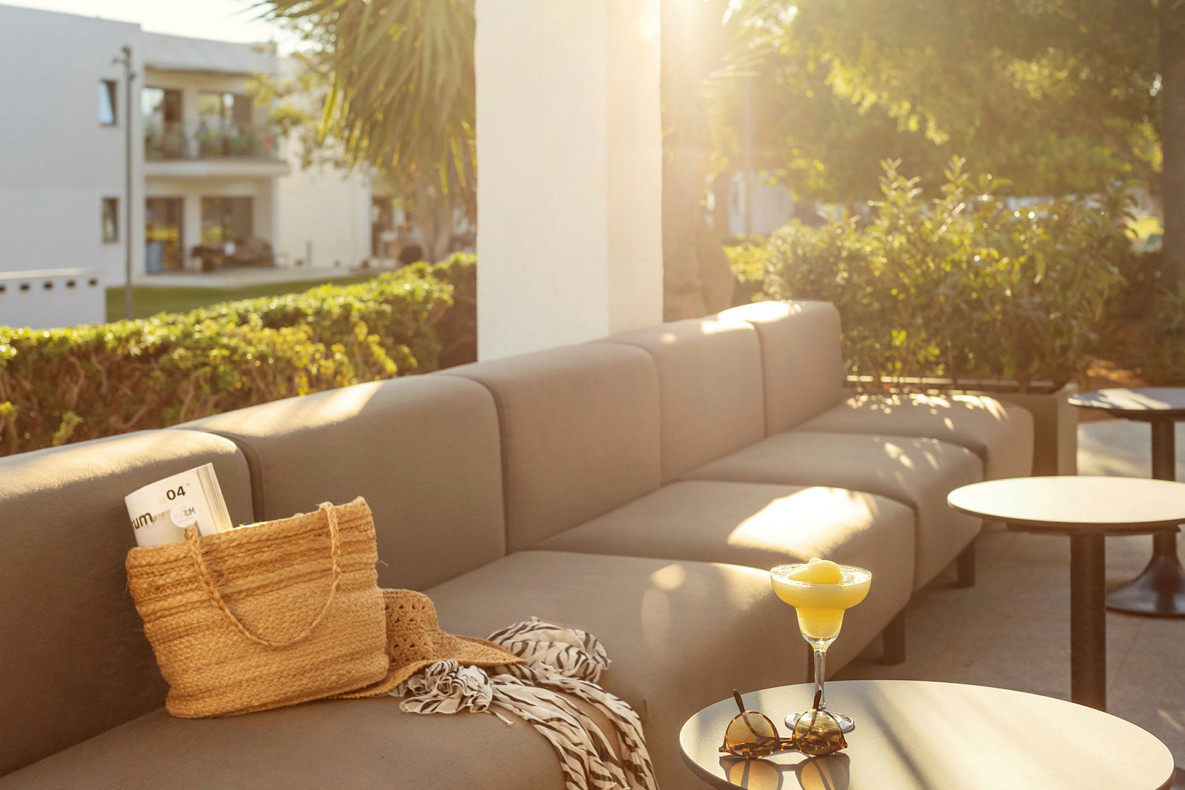 Sofa og bord på en terrasse med sollys, på bordet står et glass og solbriller. (AI-generert tekst)