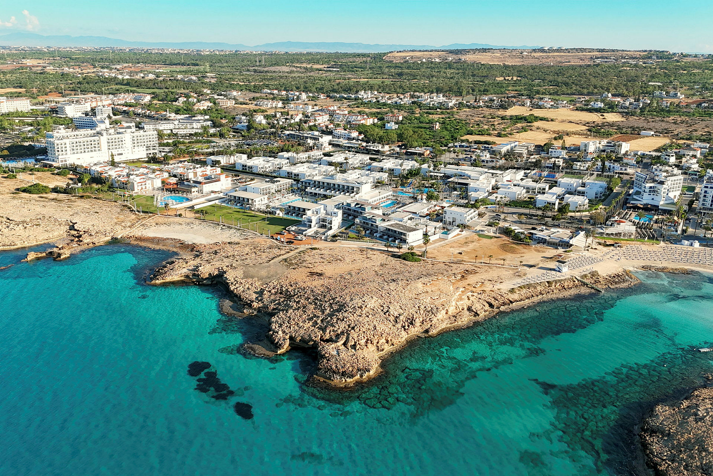 Flyfoto av kystlandskap med turkist vann og bygninger ved stranden. (AI-generert tekst)