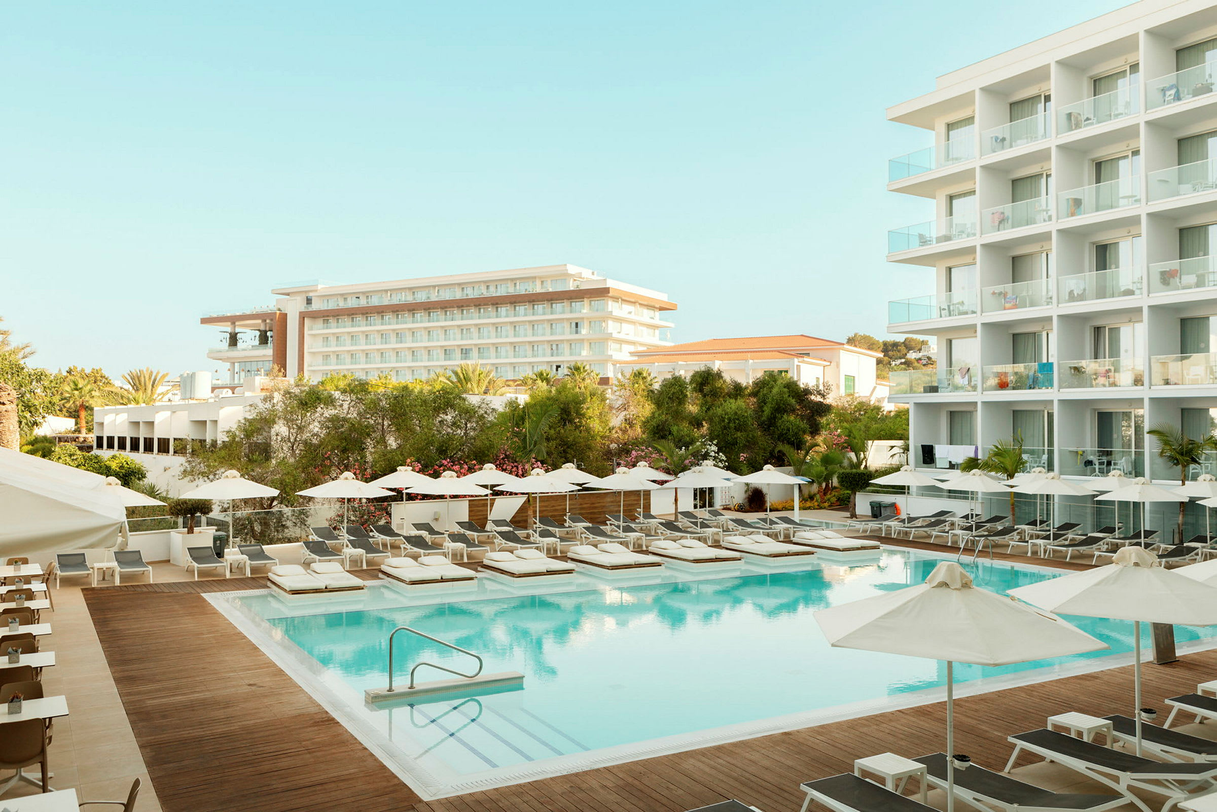 Hotellområde med basseng, solsenger og bygninger i bakgrunnen. (AI-generert tekst)