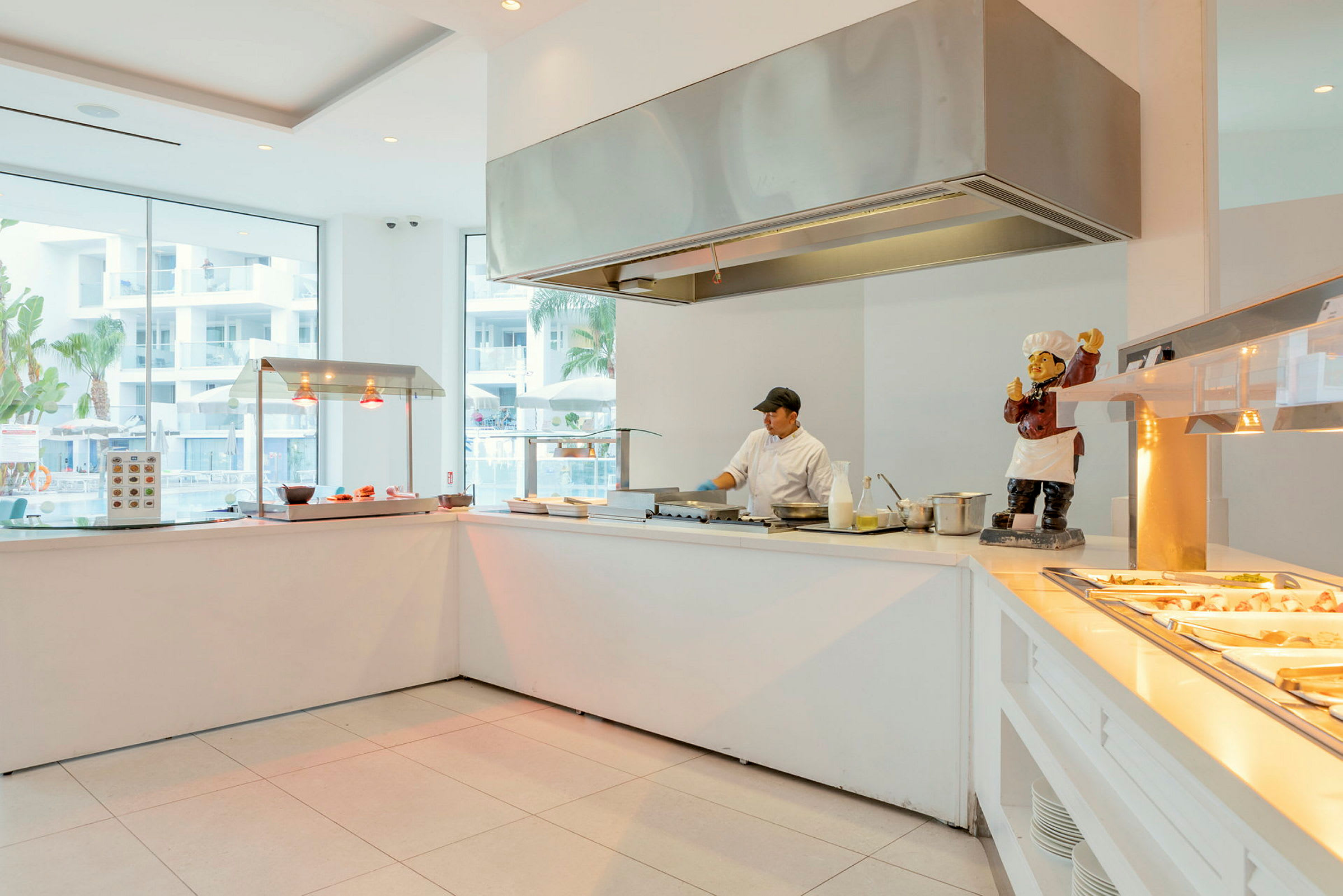 Et moderne hotellkjøkken med ulike matstasjoner ved store glassvinduer. (AI-generert tekst)