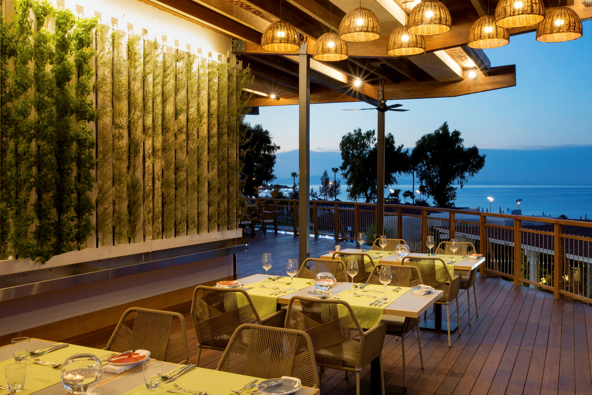 Restaurant med utendørsterrasse, bord dekket til middag og havutsikt i bakgrunnen. (AI-generert tekst)