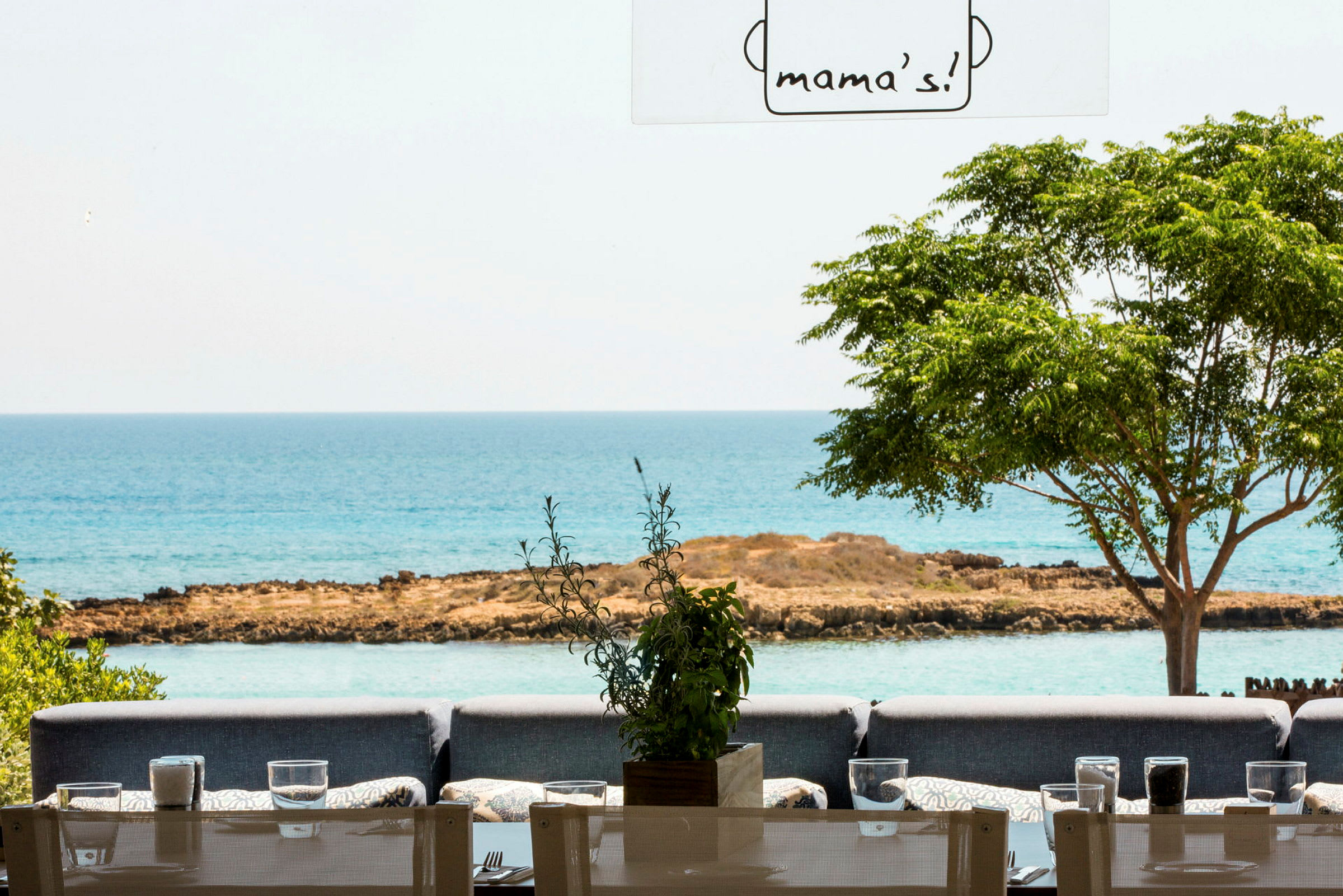 Restaurant med sitteplasser utendørs, utsikt mot havet og grøntområder. (AI-generert tekst)