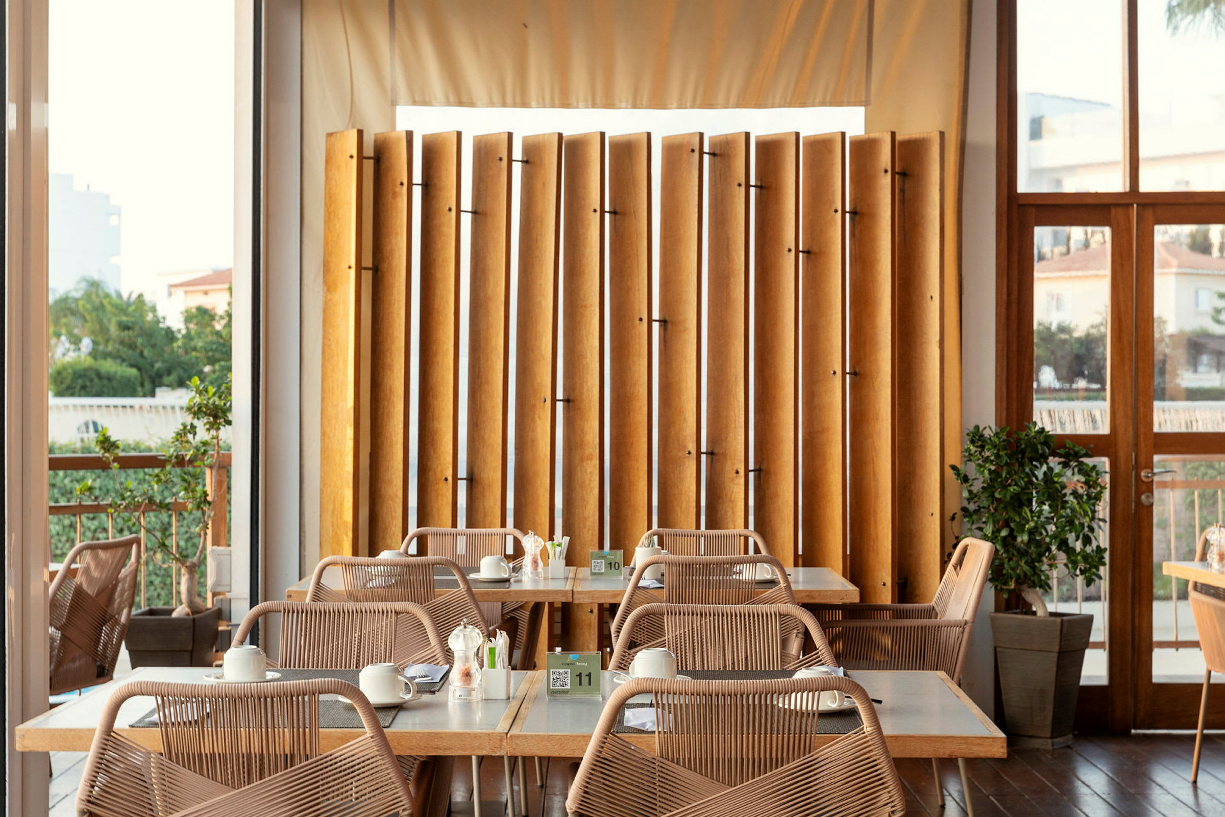 En lys restaurant med bord og stoler og horisontalt plasserte trær. (AI-generert tekst)