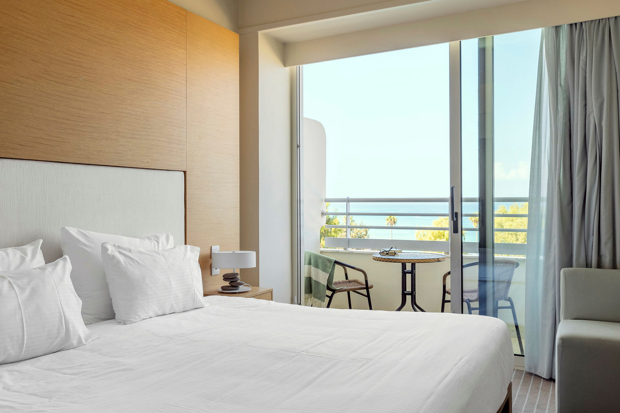 Et hotellrom med oppredd seng og en balkong med utsikt over havet. (AI-generert tekst)