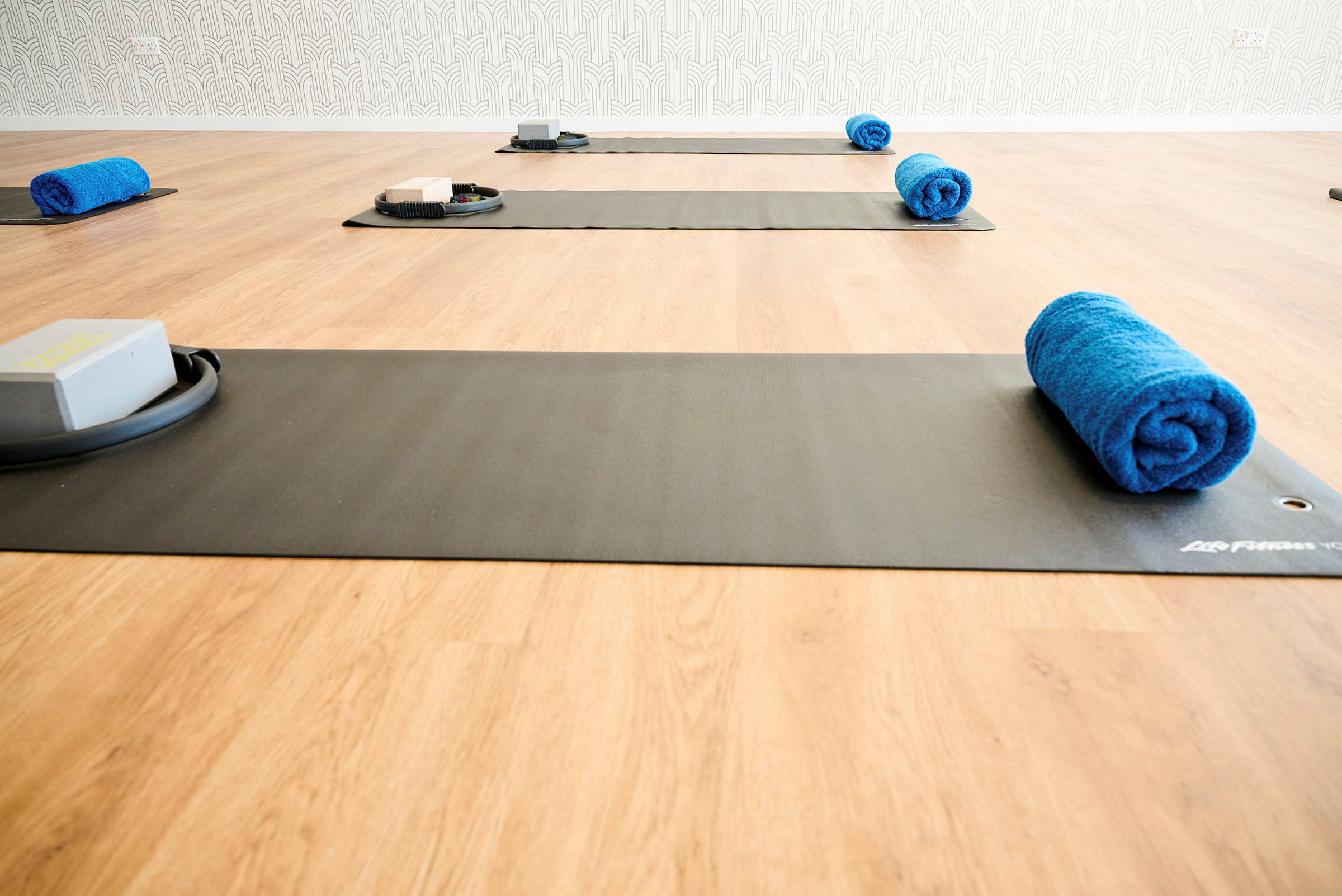 Bilde av et treningsstudio med yogamatter, blå håndklær og treningsblokker på et tregulv. (AI-generert tekst)