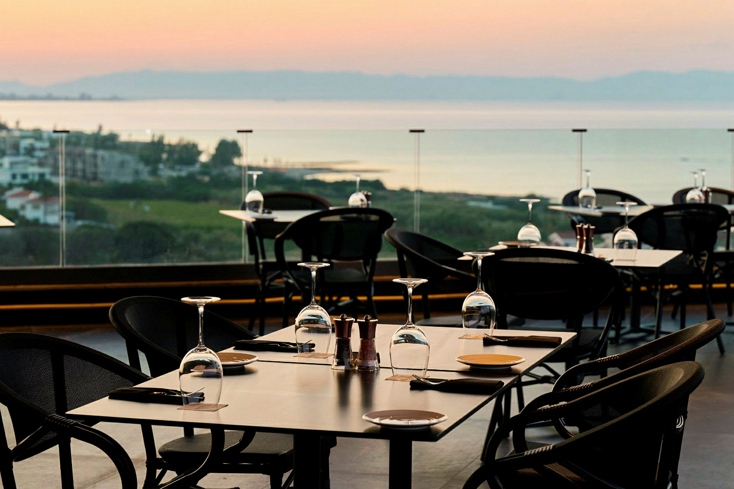 En uterestaurant med dekkede bord og utsikt over landskap og vann. (AI-generert tekst)