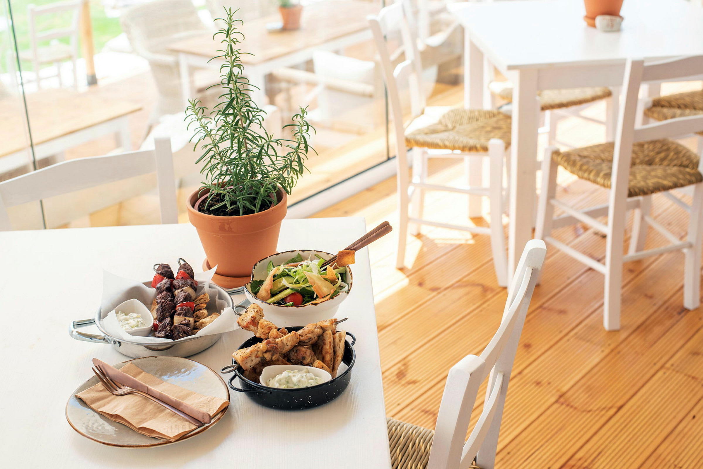 Et dekket bord med forskjellige retter, inkludert salat, grillspyd og en urteplante. (AI-generert tekst)