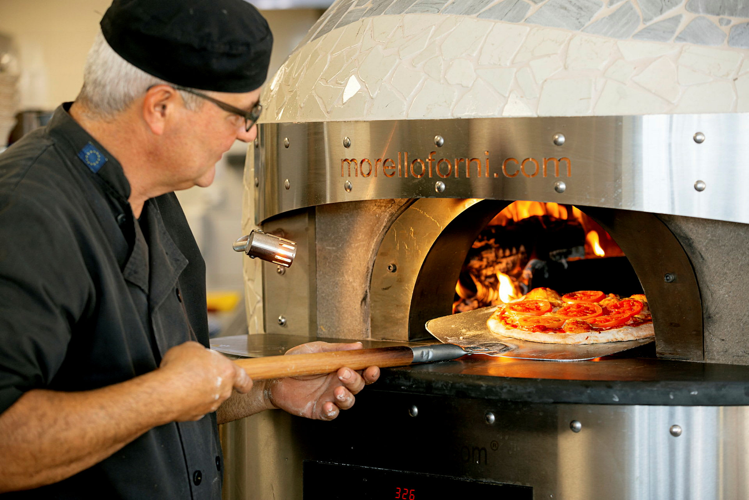 En pizza blir plassert i en vedfyrt ovn med en pizzaspade. (AI-generert tekst)