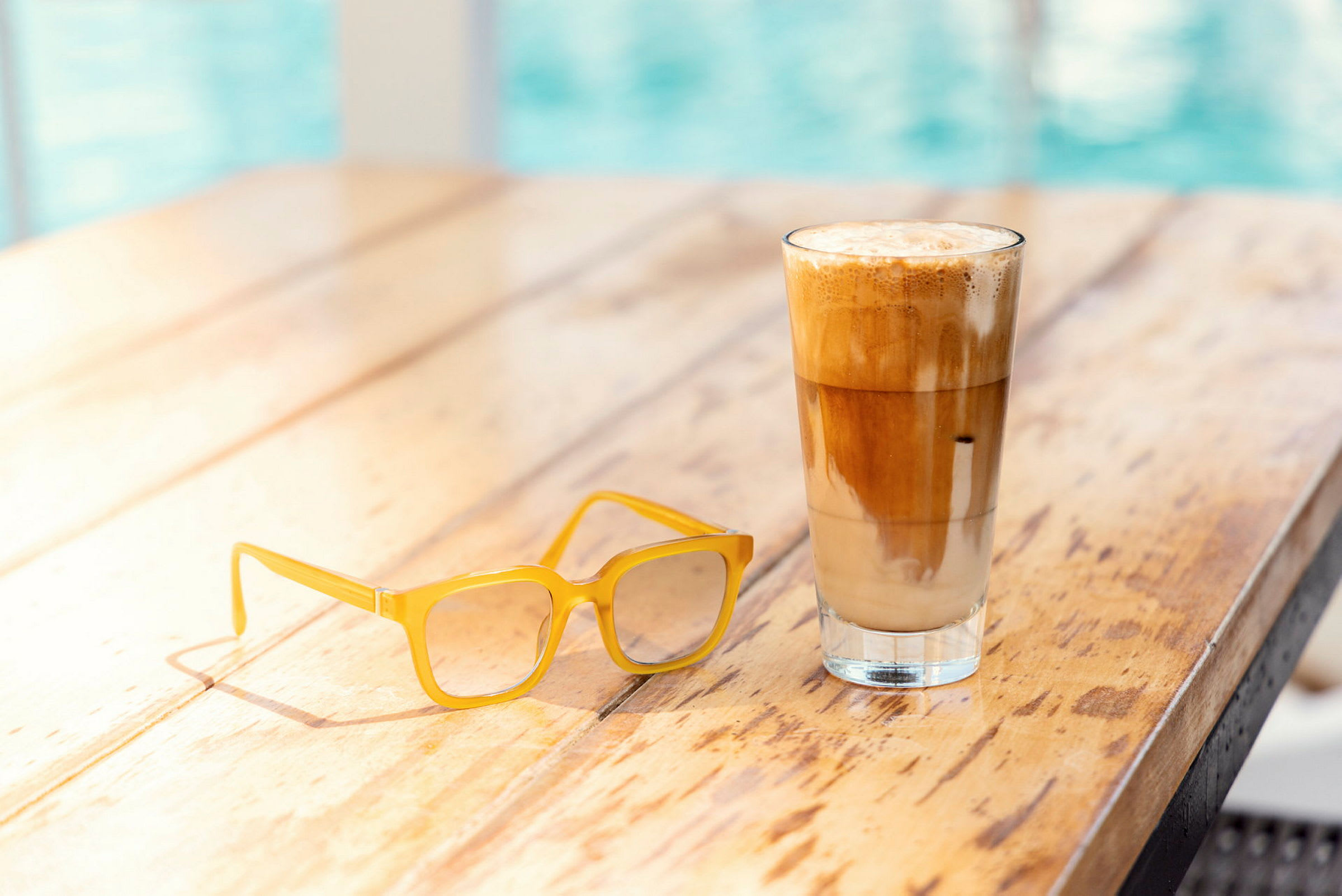 Et trebord med et par gule briller og et glass iskaffe eller latte. (AI-generert tekst)