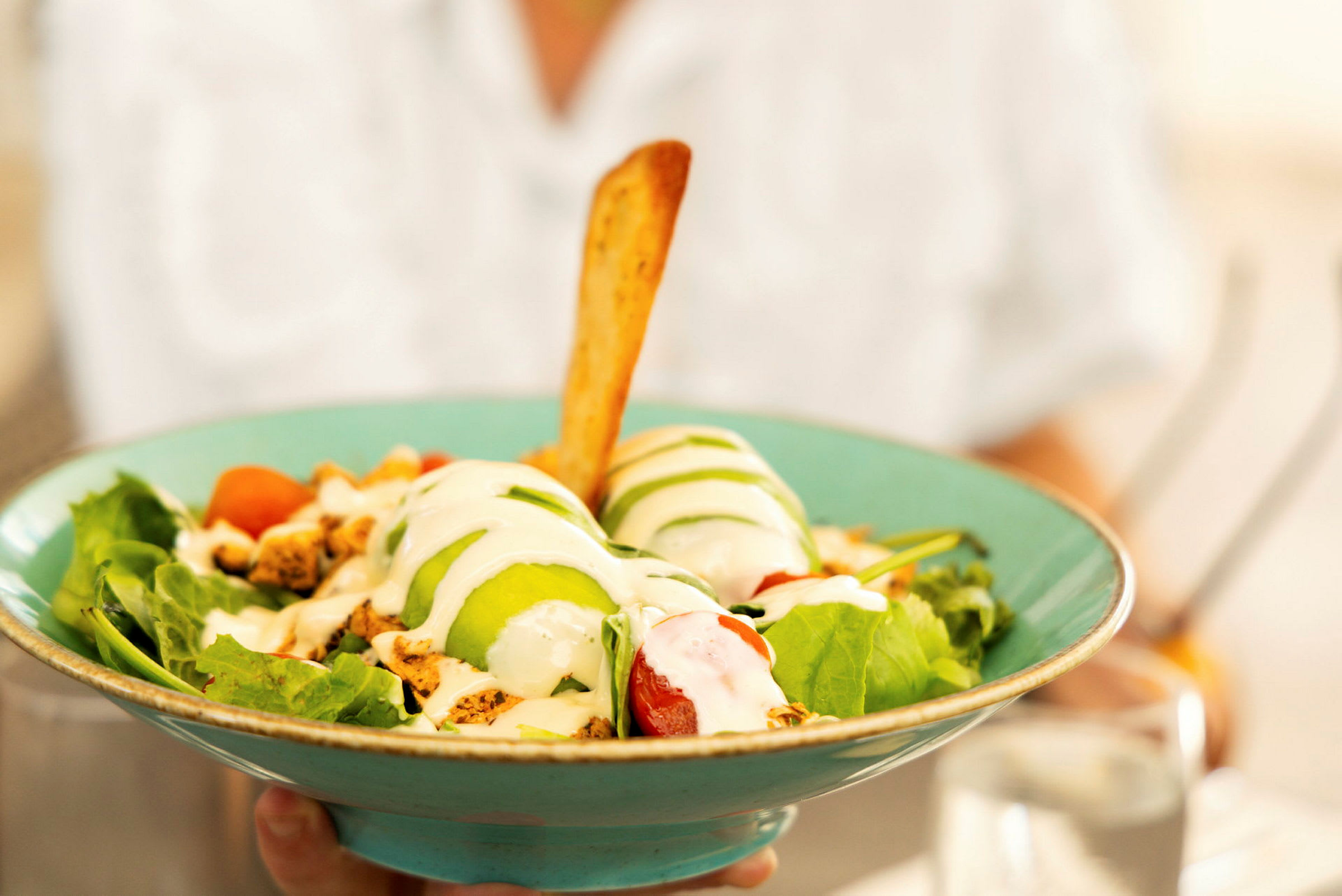 En salat servert i en turkisfarget bolle, som inneholder grønnsaker, avokado, dressing og en brødpinne. (AI-generert tekst)