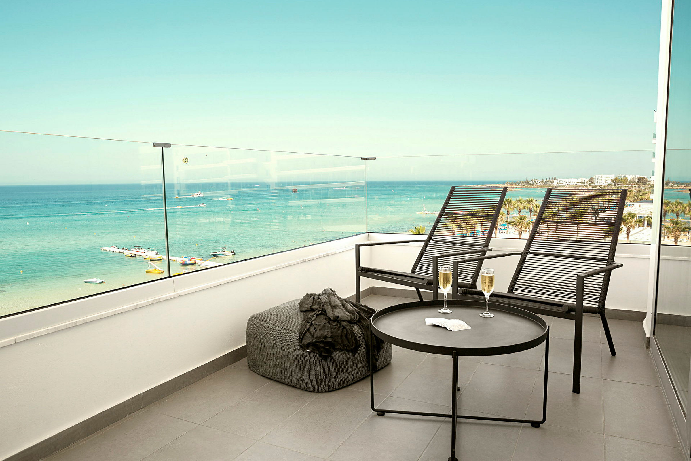 To solstoler og et bord med to glass står på en terrasse med utsikt over havet. (AI-generert tekst)