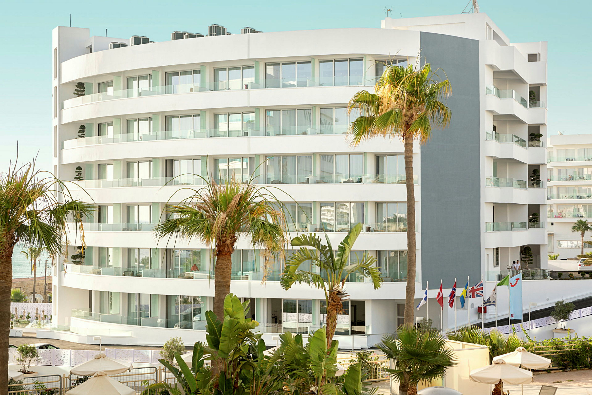 Bilde av en moderne hvit hotellbygning omgitt av palmer og vegetasjon. (AI-generert tekst)