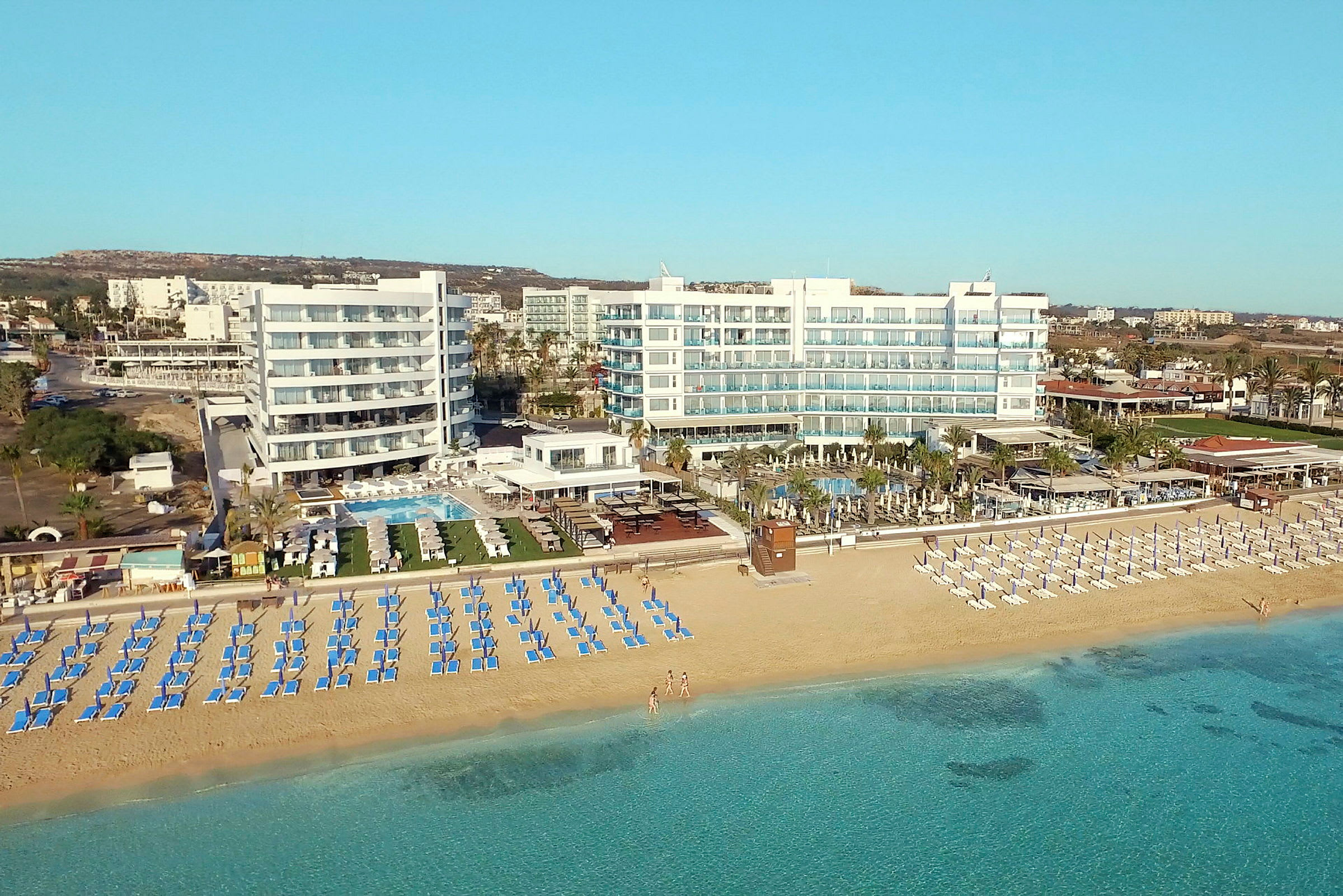 Bilde av en strand med solsenger og parasoller foran et hotell ved kysten. (AI-generert tekst)