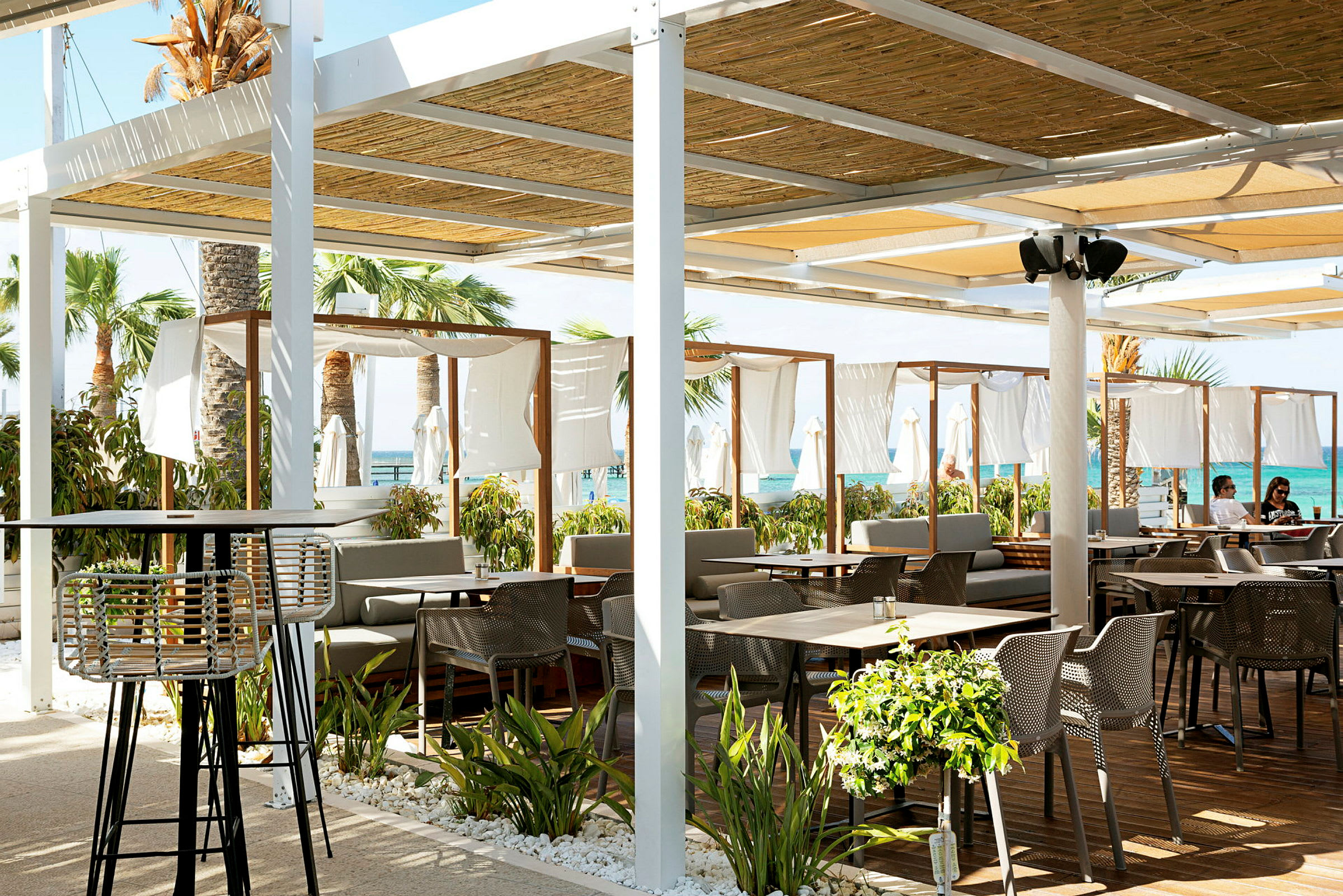 Strandnær restaurant med utemøbler og dekorativ vegetasjon. (AI-generert tekst)