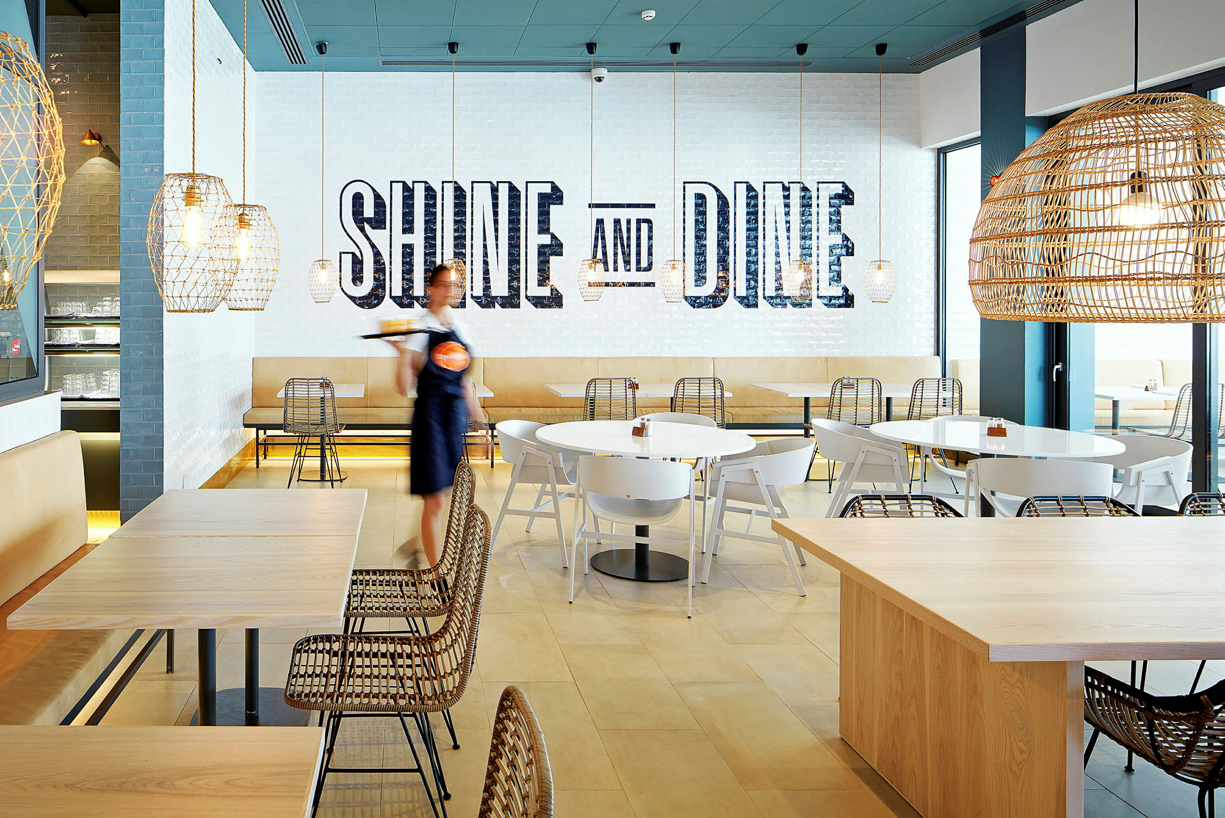En moderne restaurant med sitteplasser, belysning og tekst på veggen som sier 'Shine and Dine'. (AI-generert tekst)