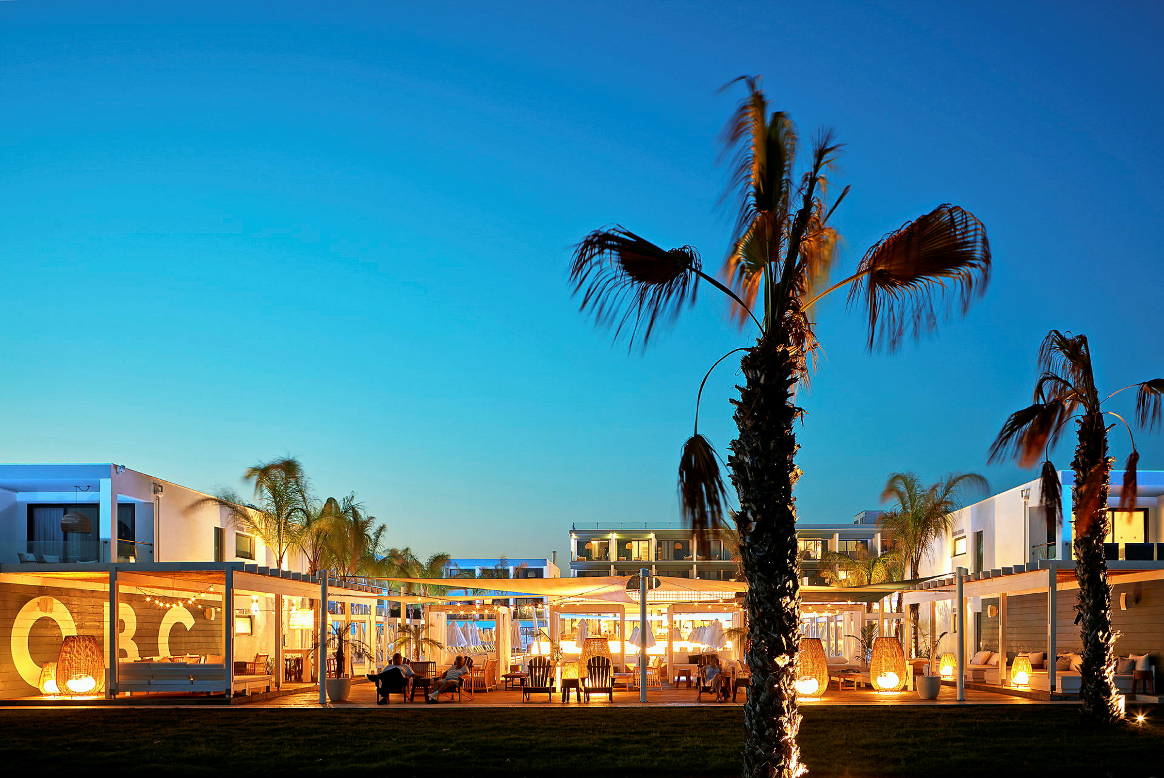 Hotellområde med palmer og opplyste bygninger i kveldslys. (AI-generert tekst)